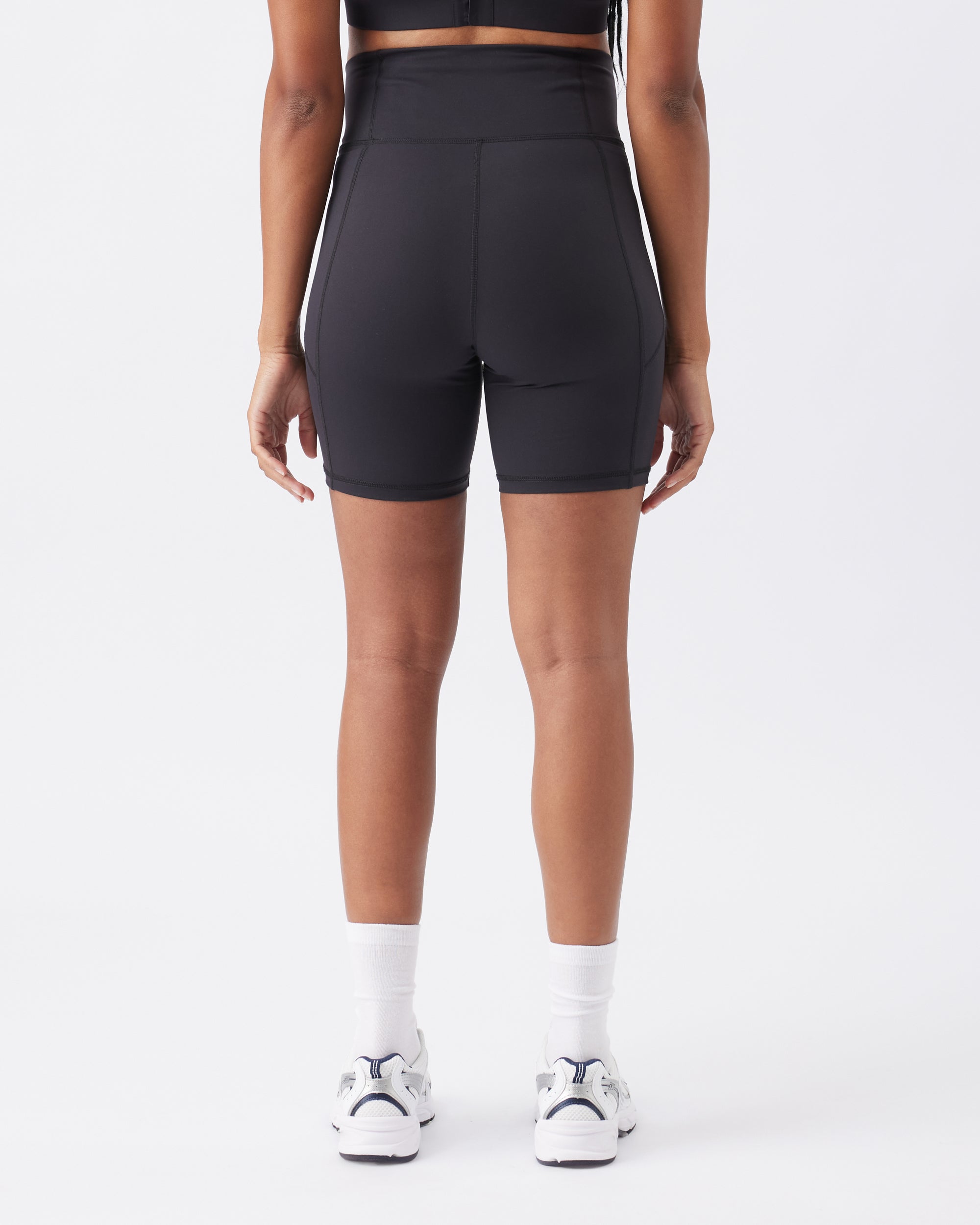 Back view of a woman wearing black athletic shorts on a white background