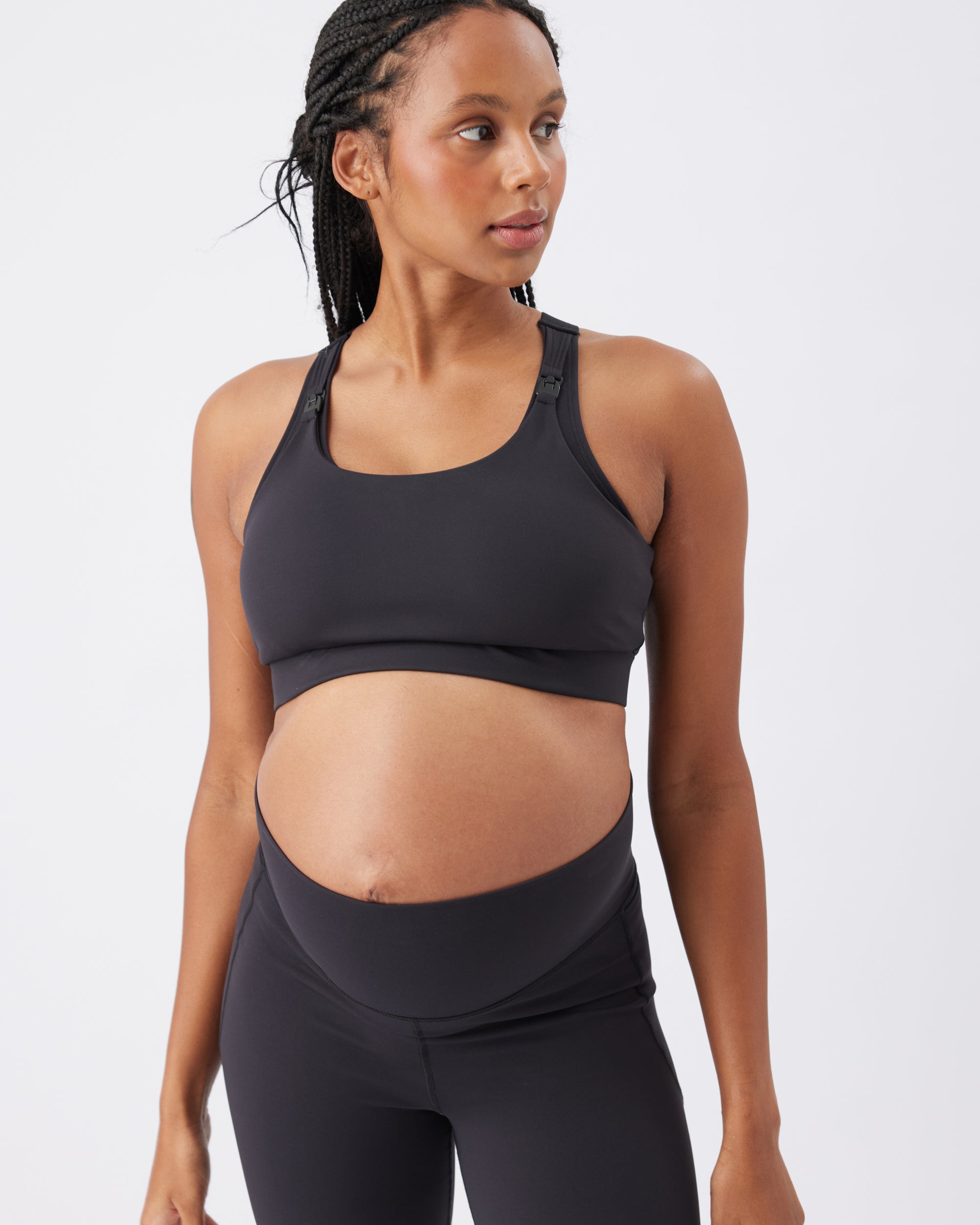 Pregnant woman wearing a black sports bra and black leggings on a white background