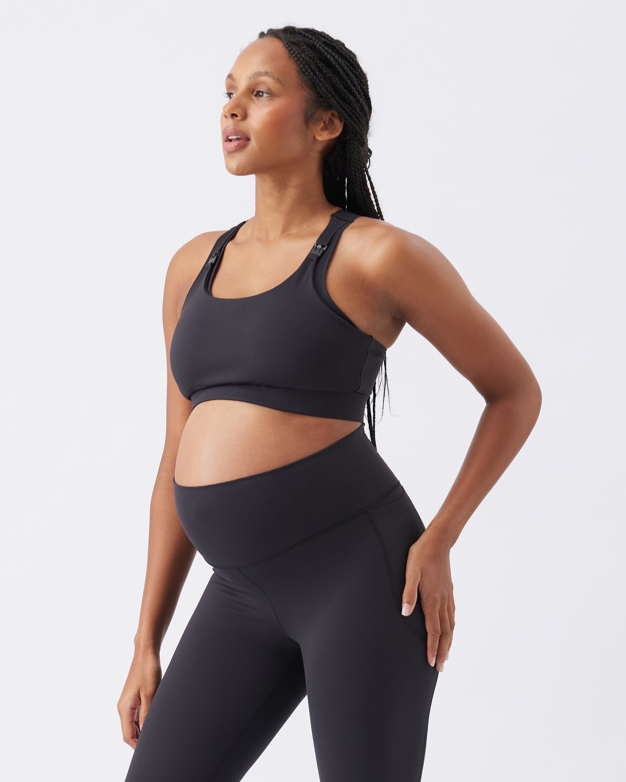Pregnant woman wearing a black sports bra and leggings on a white background