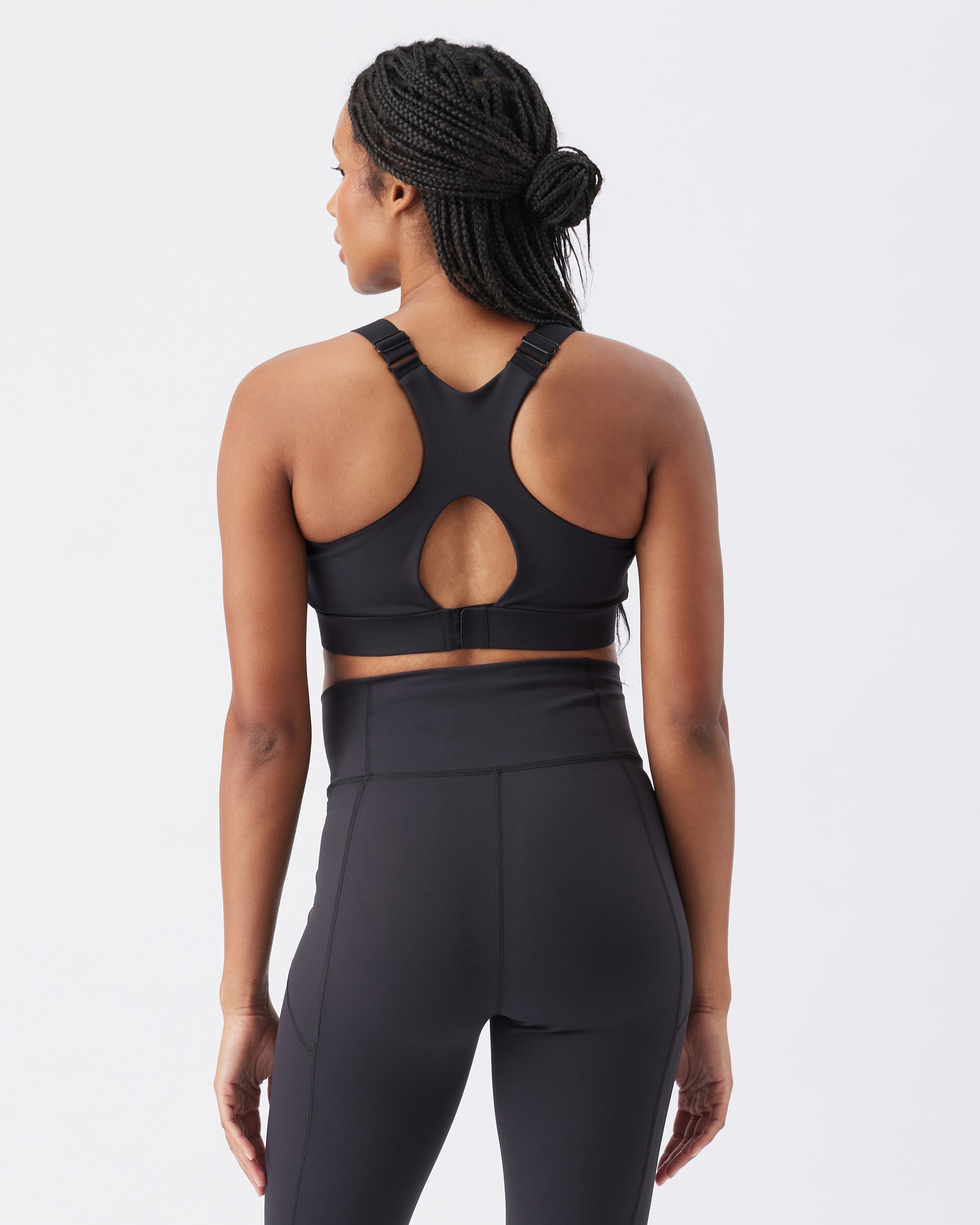Back view of a woman wearing a black sports bra and leggings on a white background