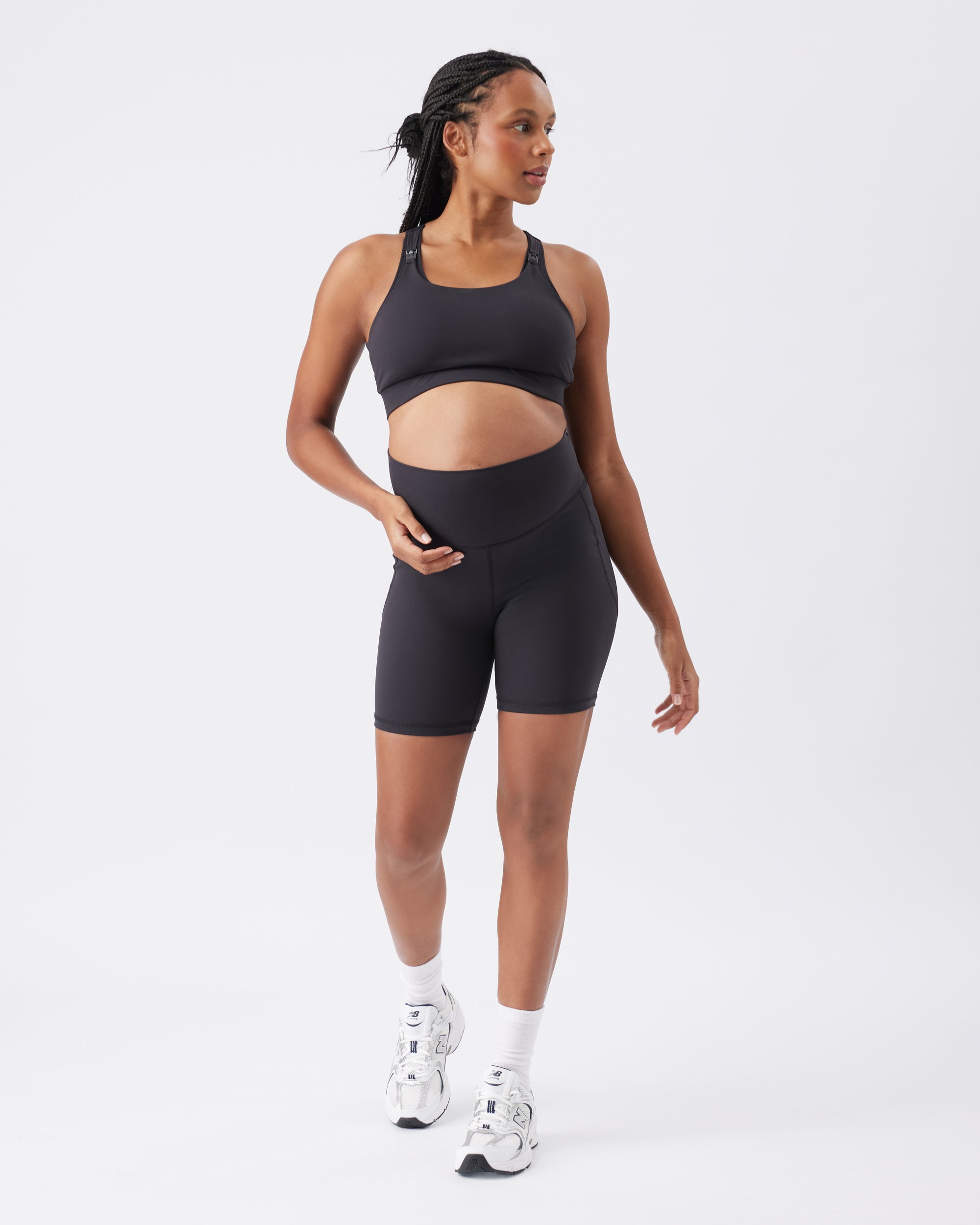 Full view of a pregnant woman wearing a black athletic outfit on a white background