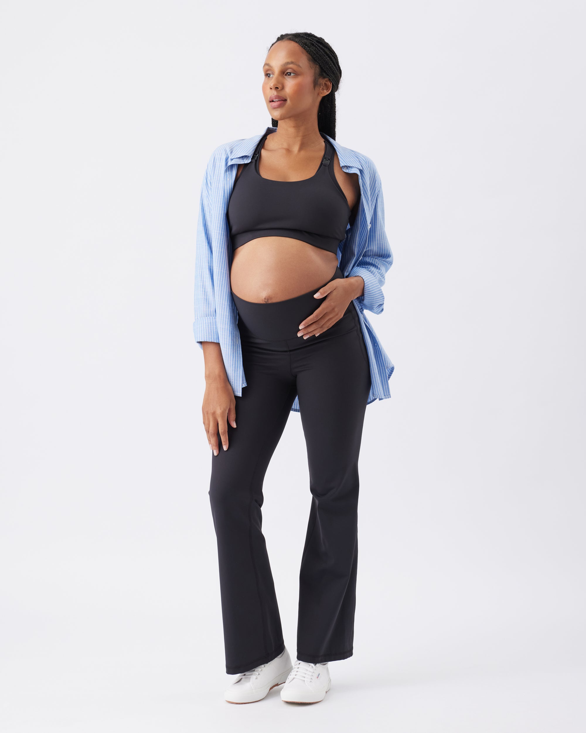 Woman wearing a blue open shirt, black crop top and black active pants on a white background