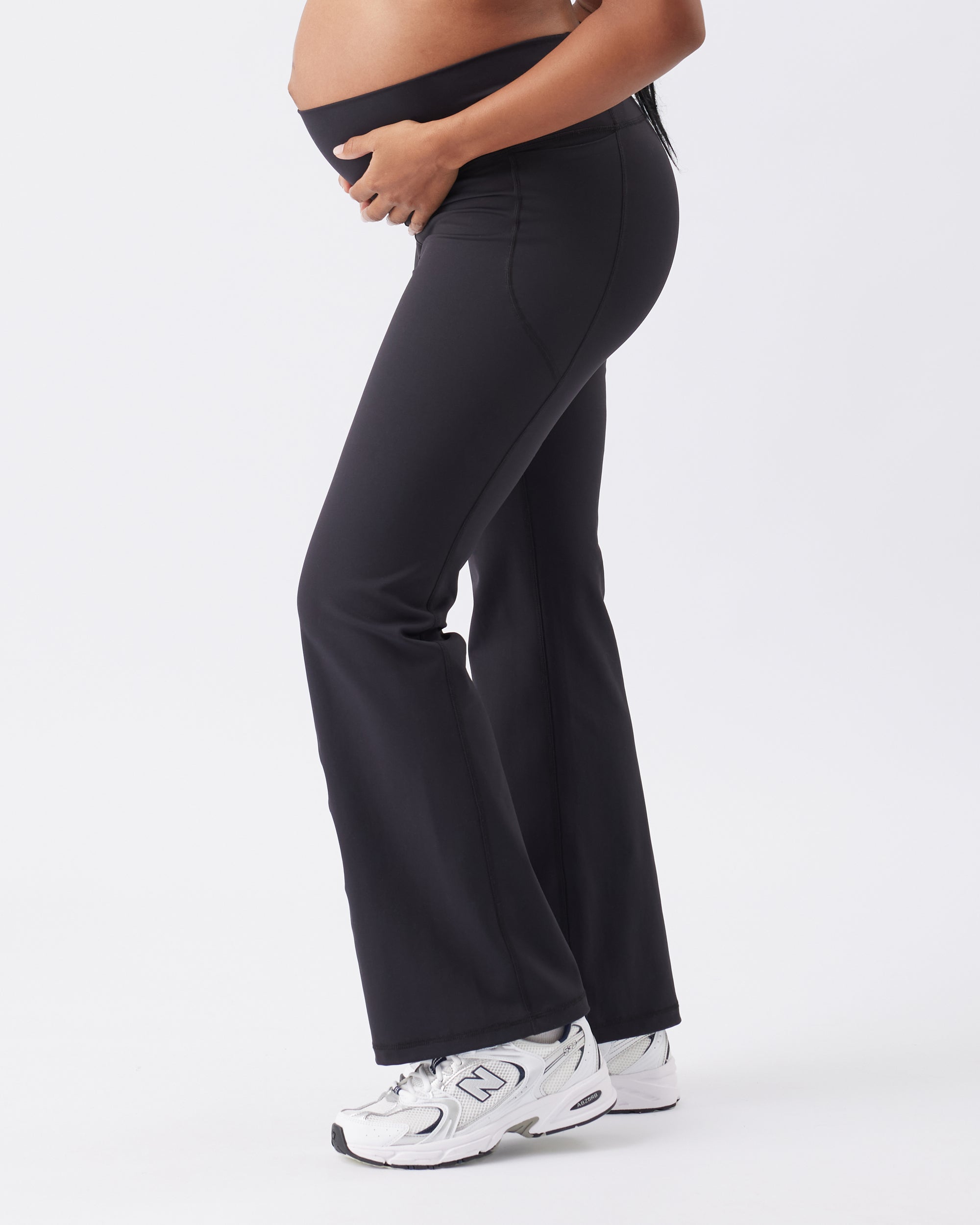 Side view of a pregnant woman wearing black maternity pants on a white background