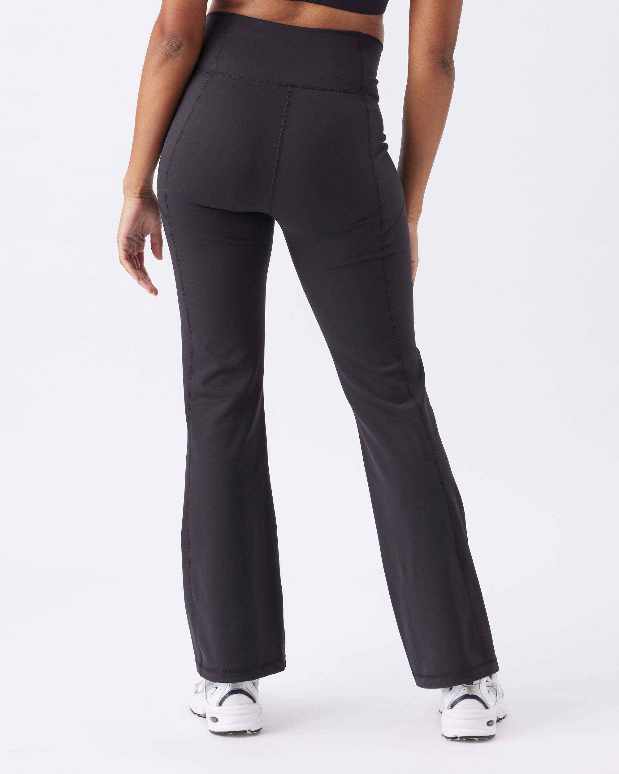Back view of a woman wearing black leggings with a white top on a light gray background