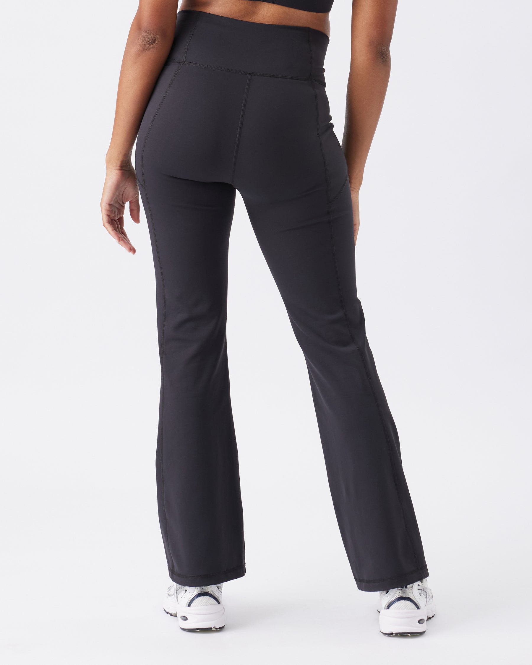 Back view of a woman wearing black leggings with a white top on a light gray background