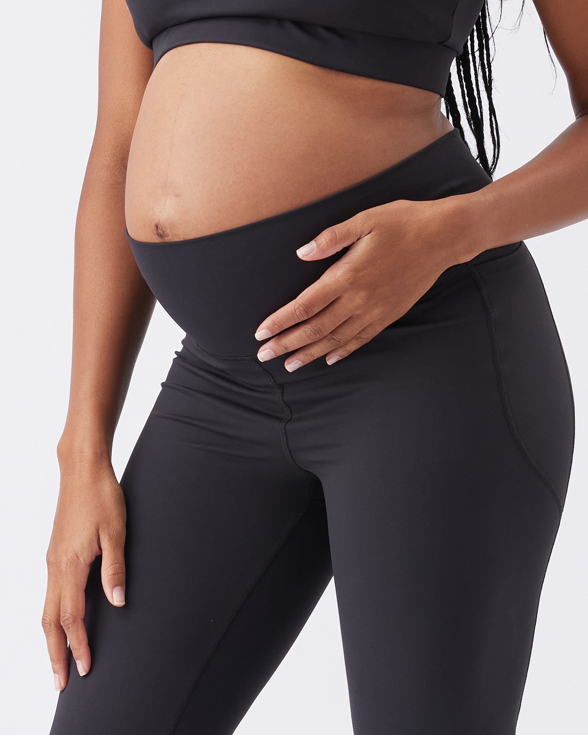 Pregnant woman wearing black leggings with a wide band on a plain background