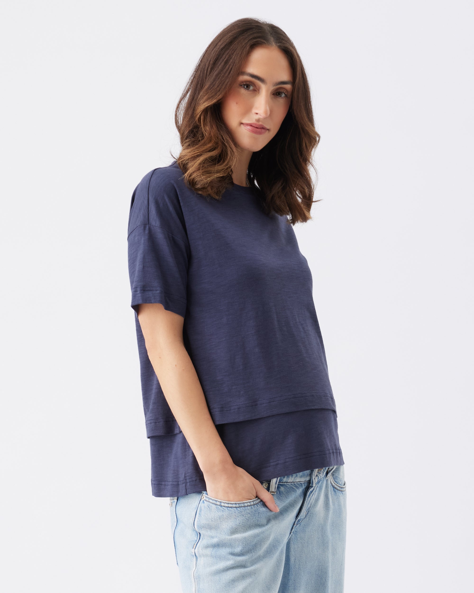 Woman wearing a navy blue nursing friendly t-shirt and light blue jeans on a white background
