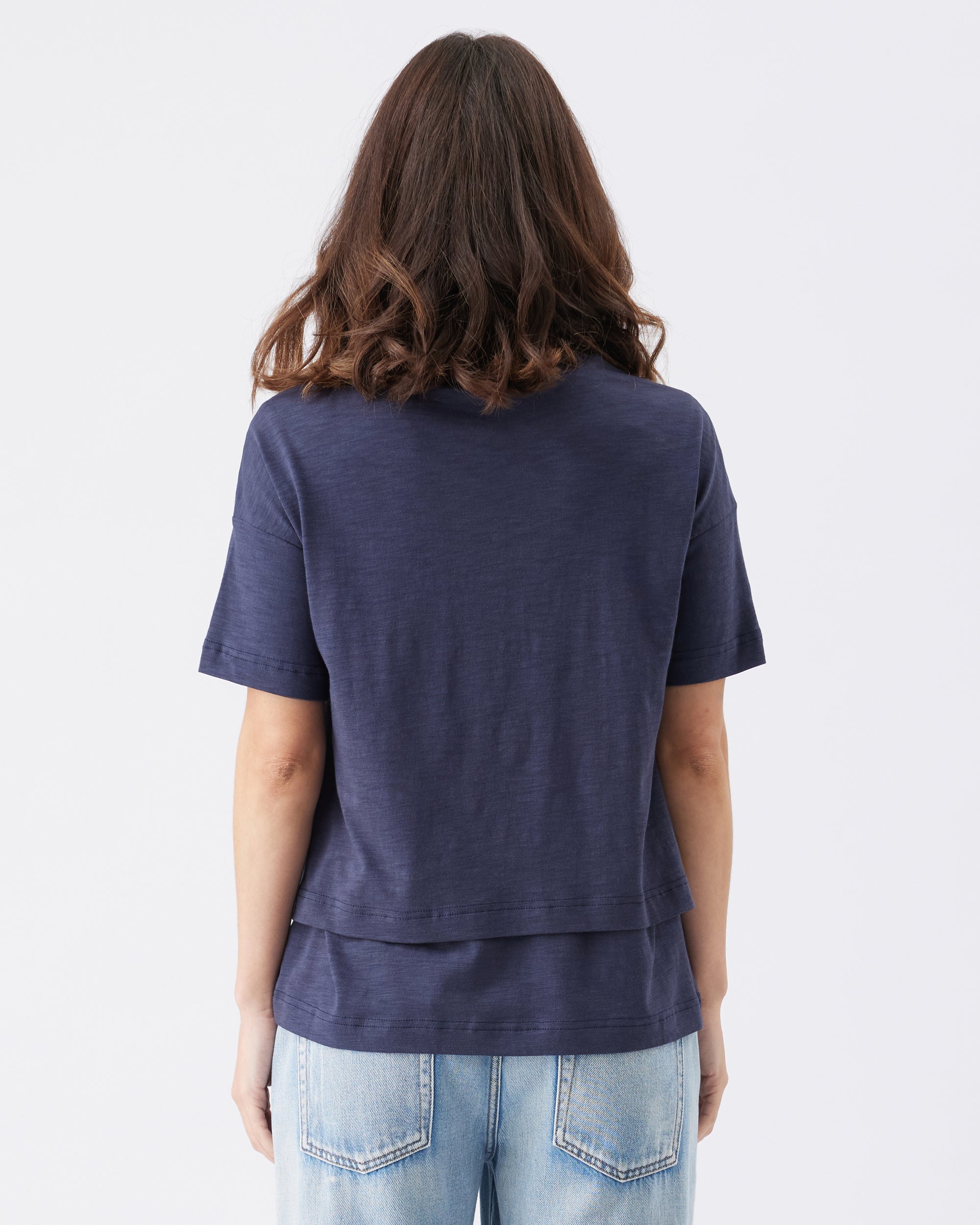 The back biew of a person wearing a navy blue t-shirt and light blue jeans on a white background