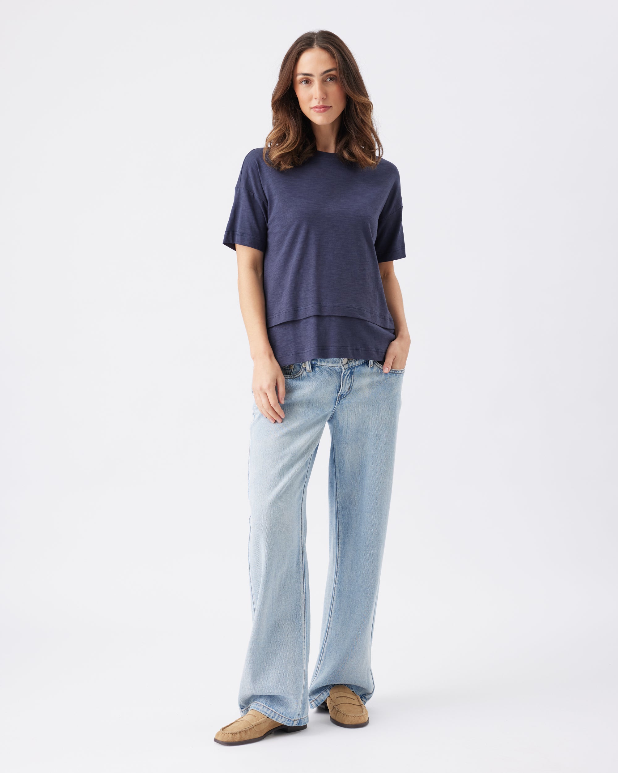 Woman wearing a navy blue top and light blue jeans on a white background
