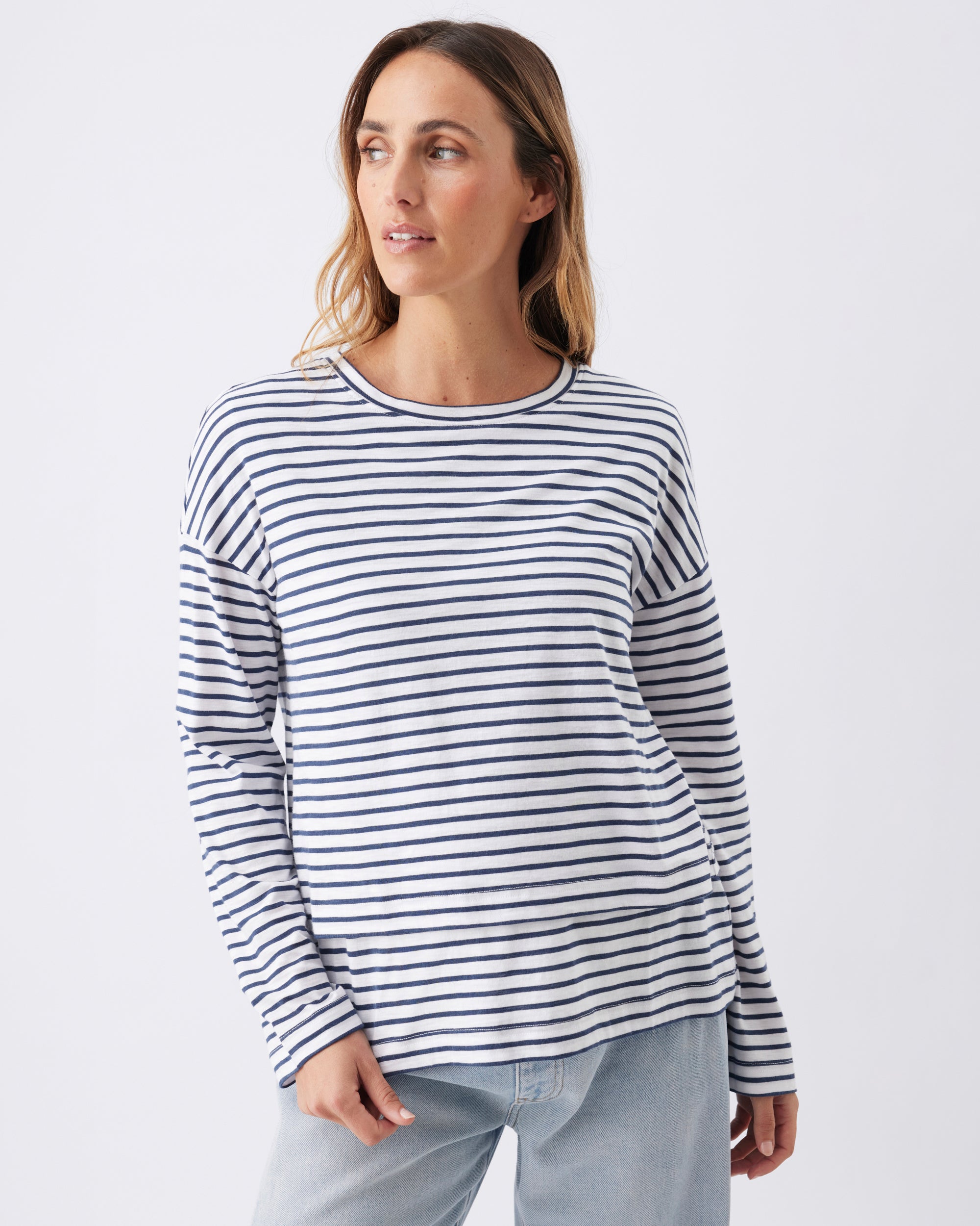 Pregnant woman wearing a Ripe Maternity navy blue and white striped long-sleeve top with jeans.