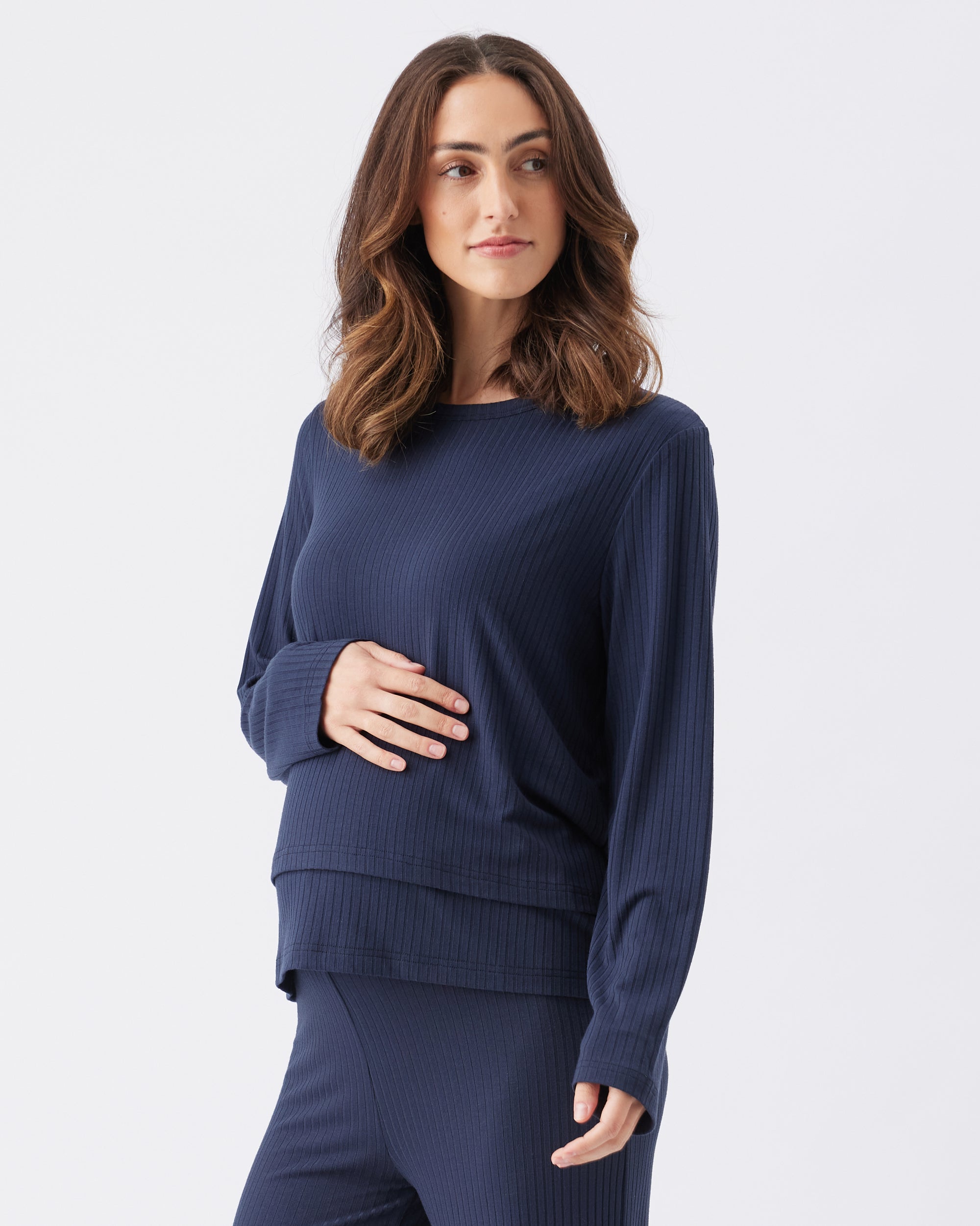 Side view of a pregnant woman wearing a navy blue sweater and pants on a white background