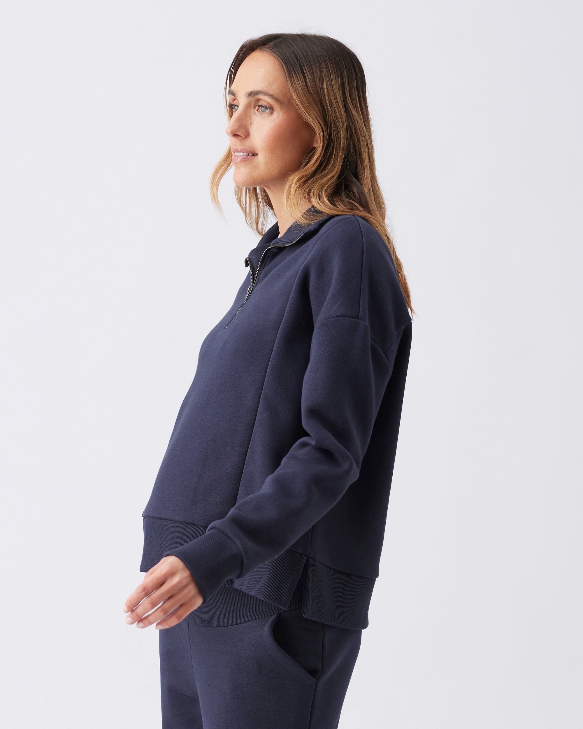 Side view of a woman wearing a navy blue sweatshirt against a white background