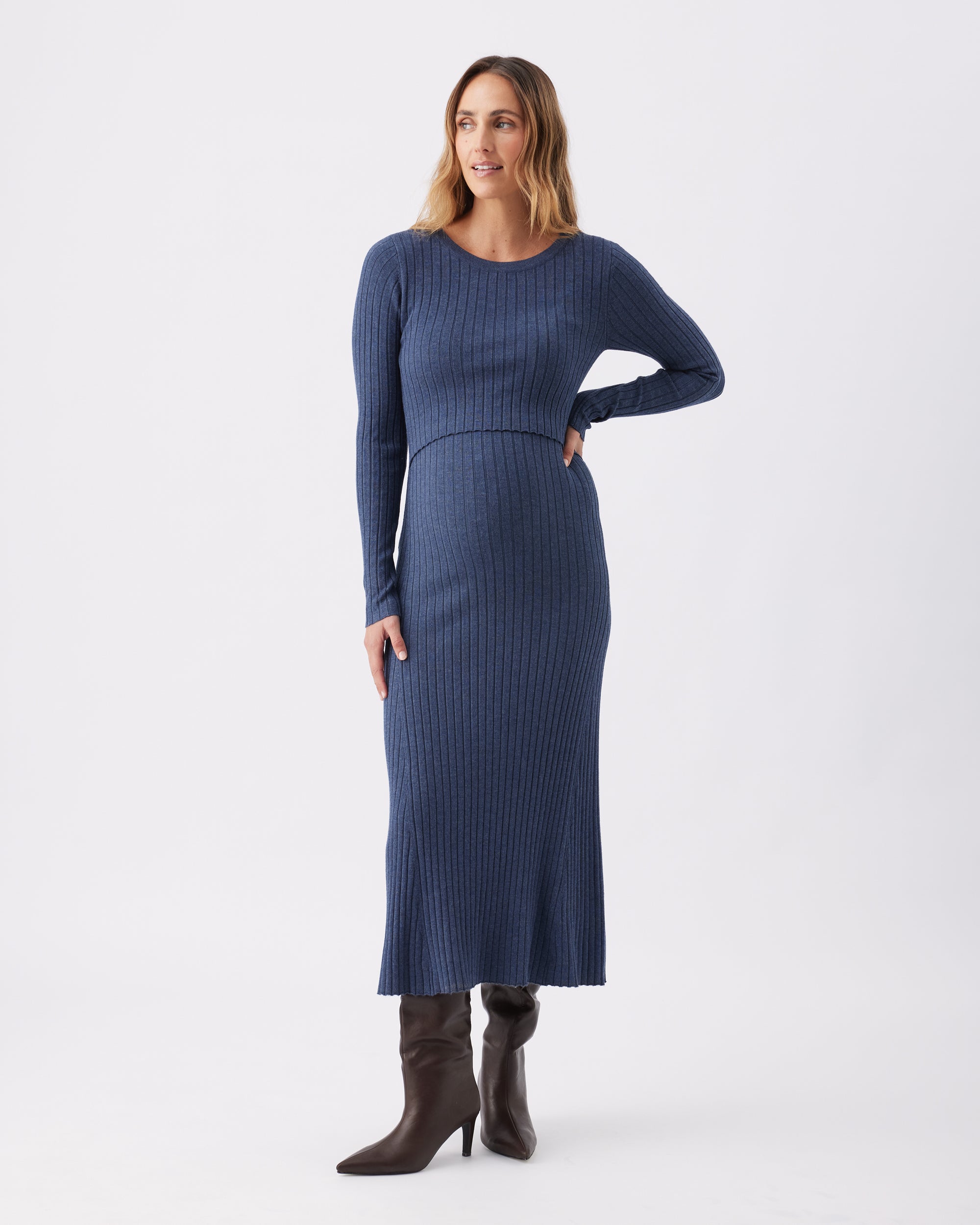 Woman wearing a Ripe Maternity blue ribbed knit long sleeved dress with brown heeled boots.