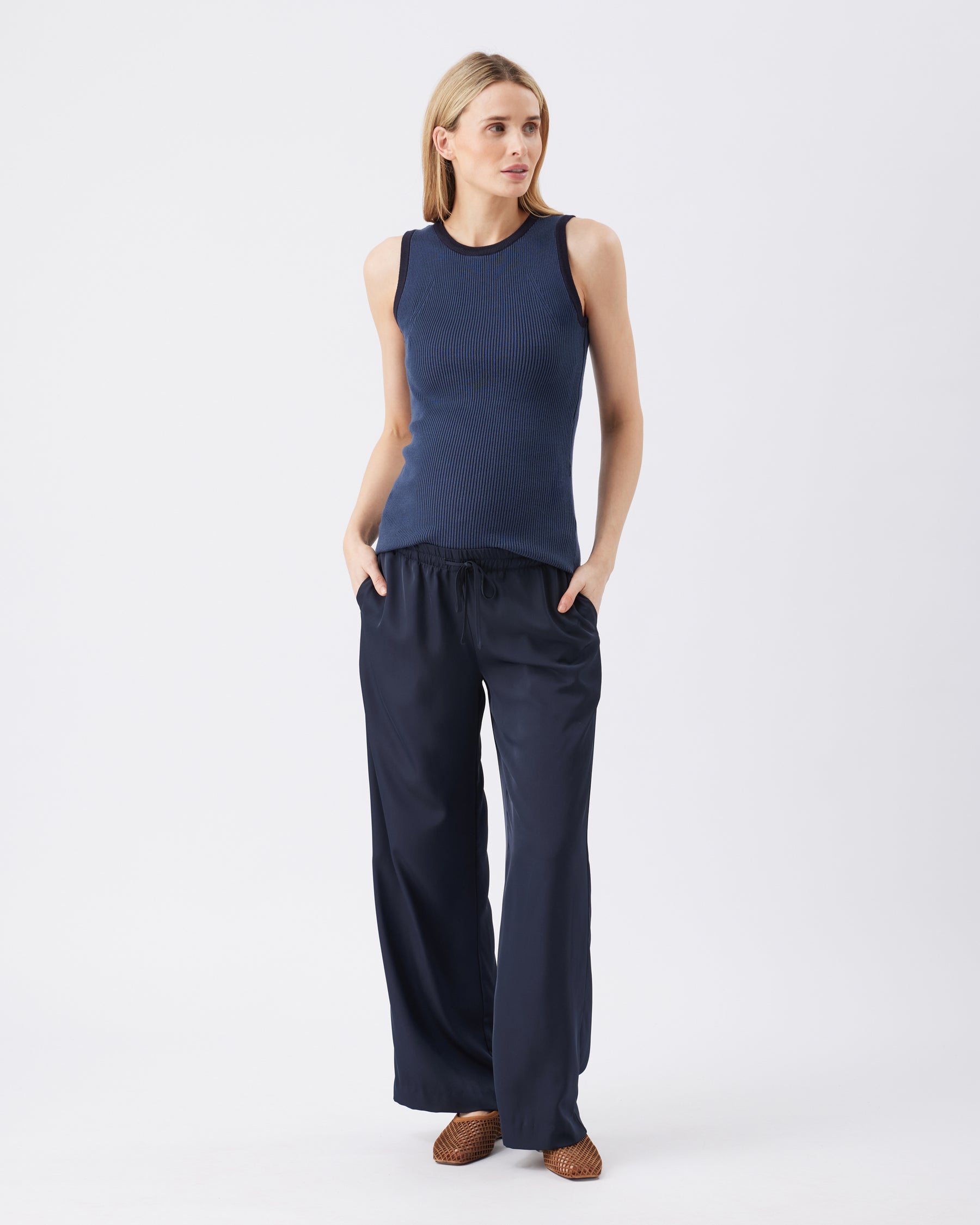 Woman wearing a navy sleeveless top and wide-leg pants on a white background