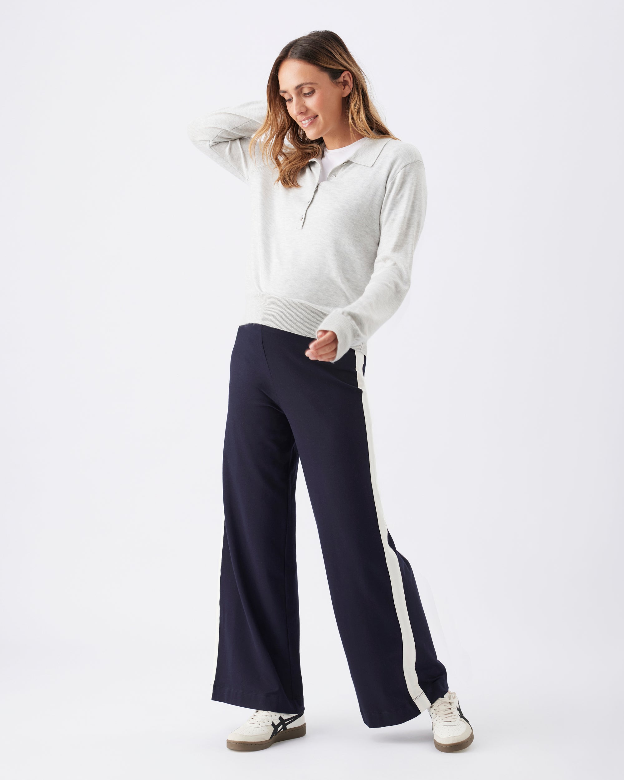 Woman wearing a light grey sweater and navy pants with a white side stripe and sneakers