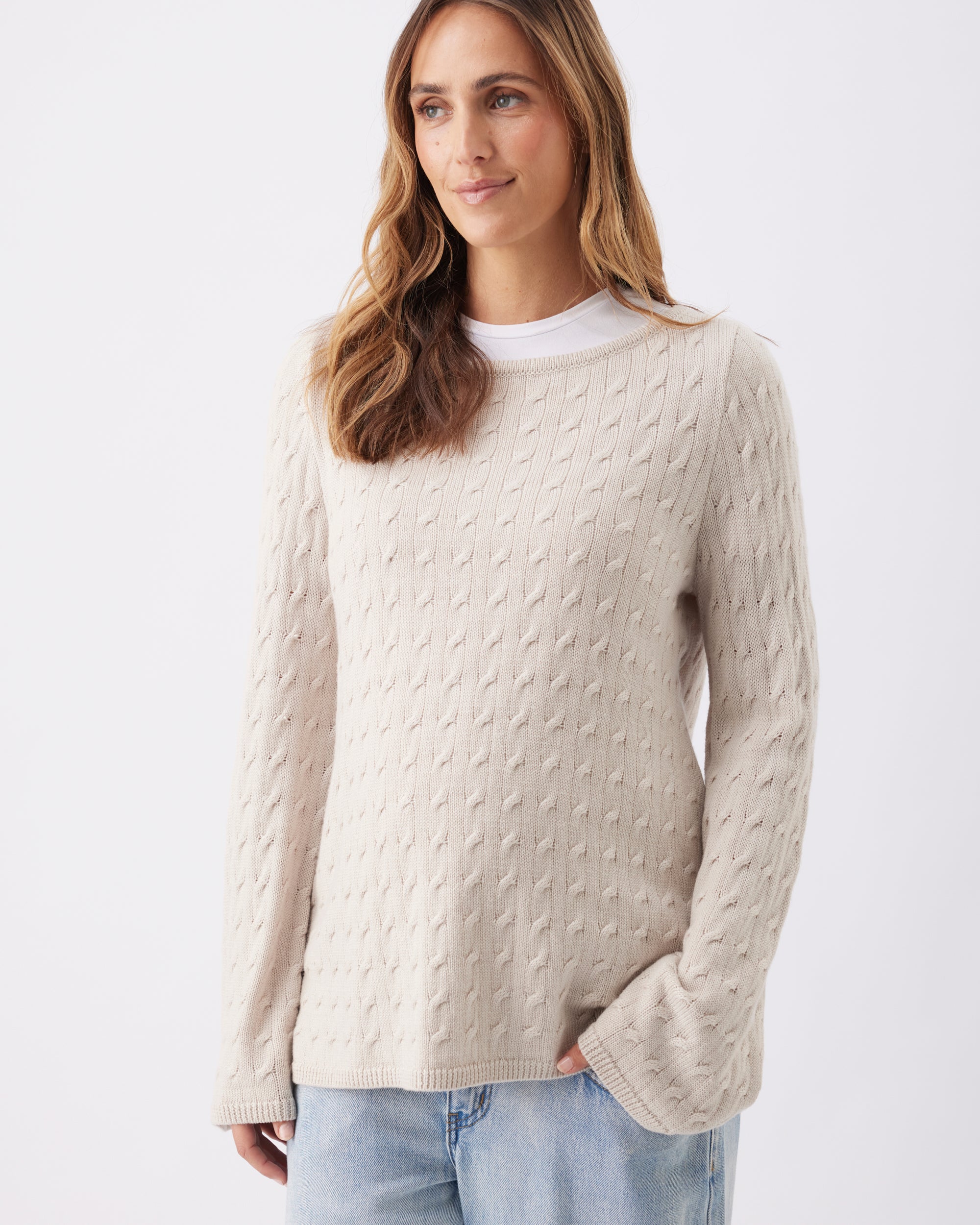 A pregant woman wearing a beige cable knit sweater with light blue jeans