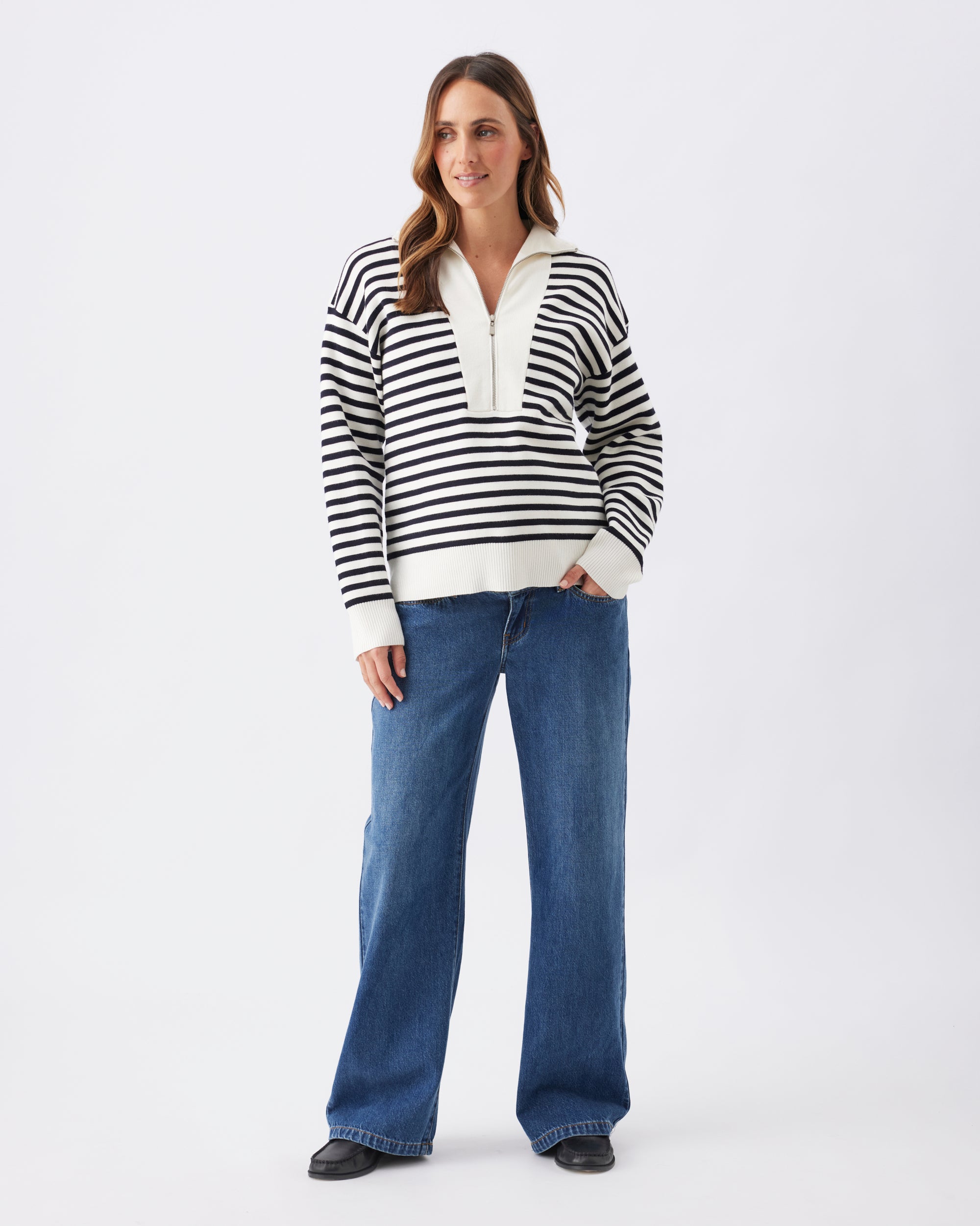 Full length view of a woman wearing a midnight blue and white striped knit, with blue jeans and black shoes on a white background.