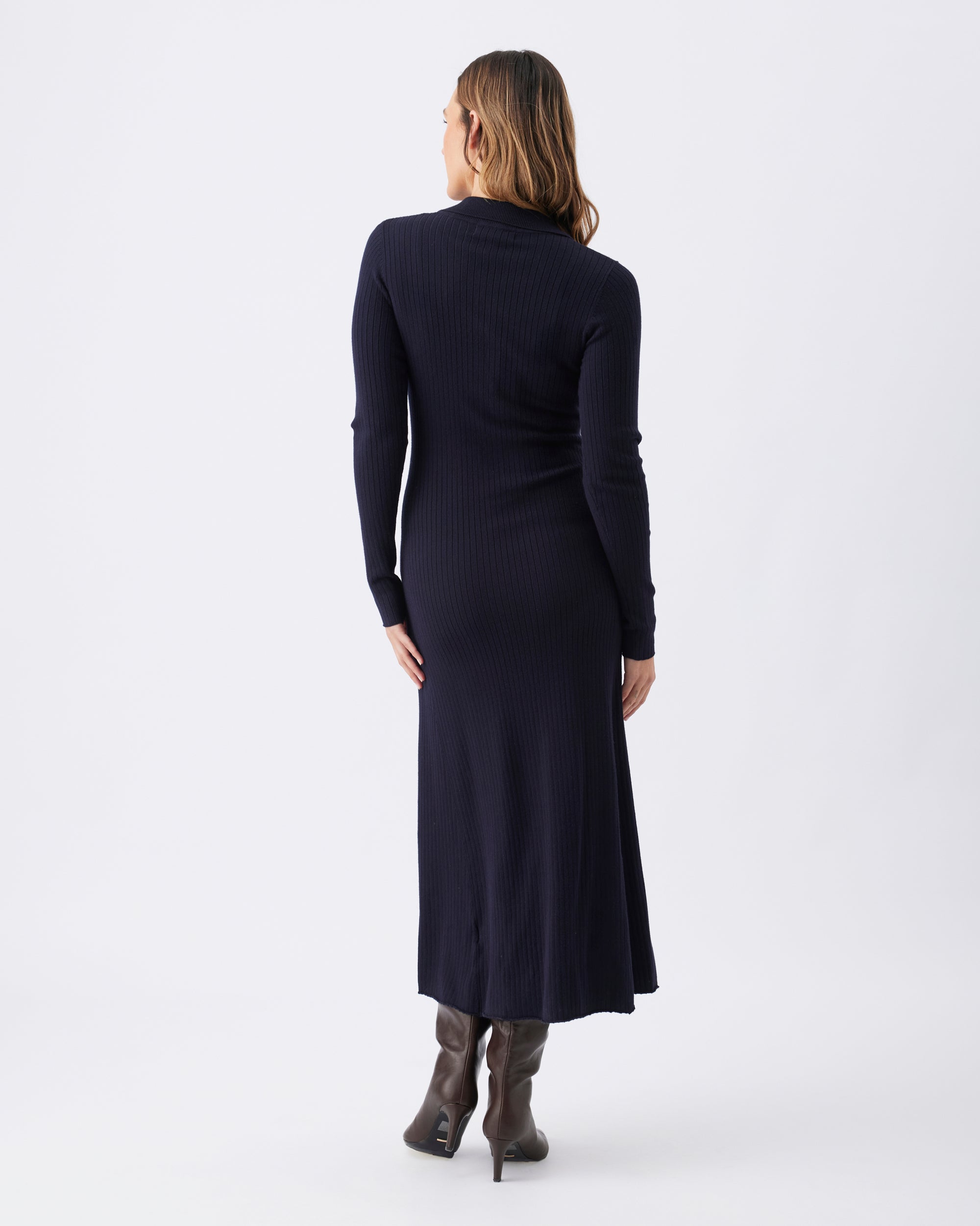 Back view of a woman wearing a long navy dress with long sleeve, and brown heeled boots.