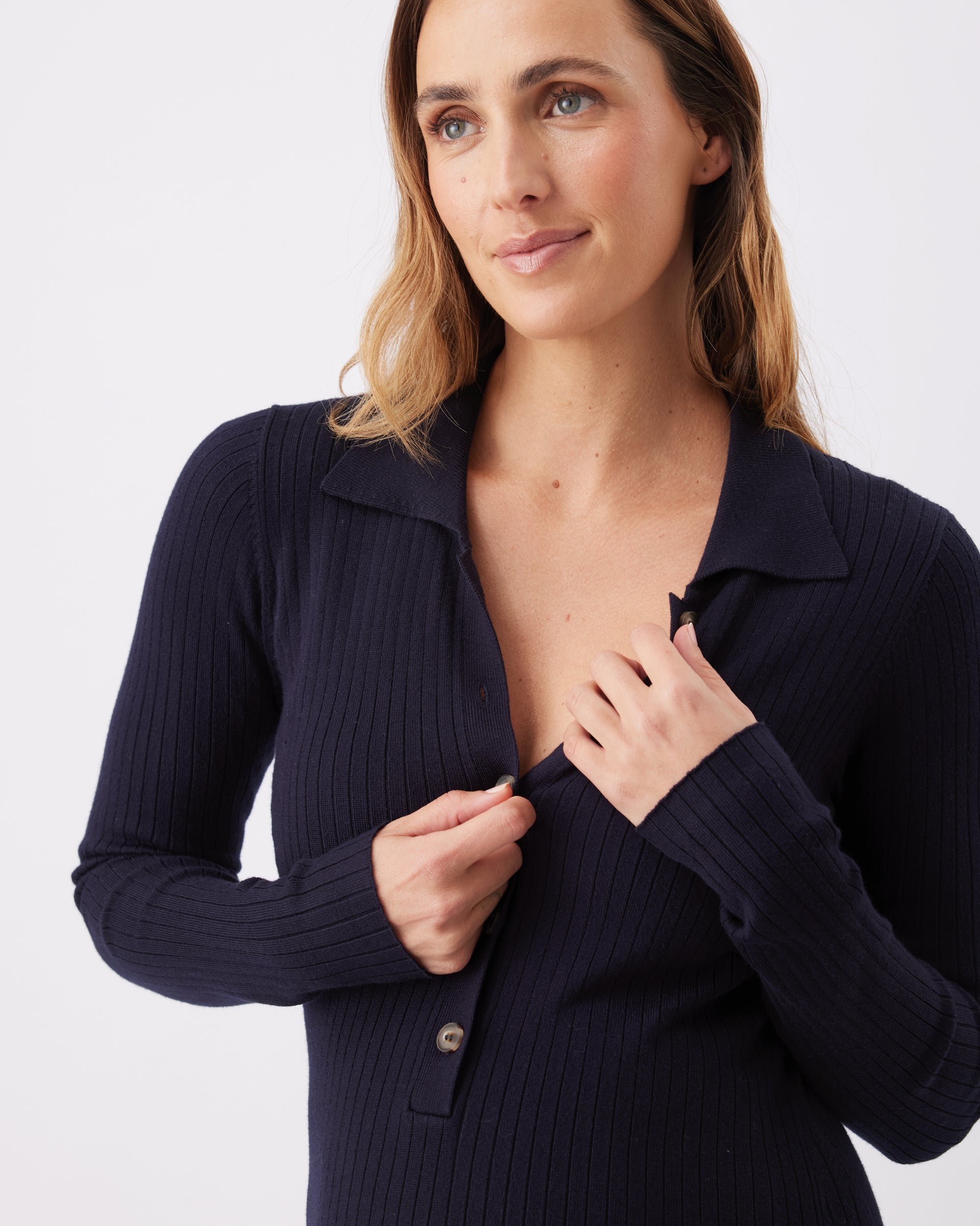 Woman wearing a dark blue ribbed long sleeve midi dress with a button up neckline and collar.