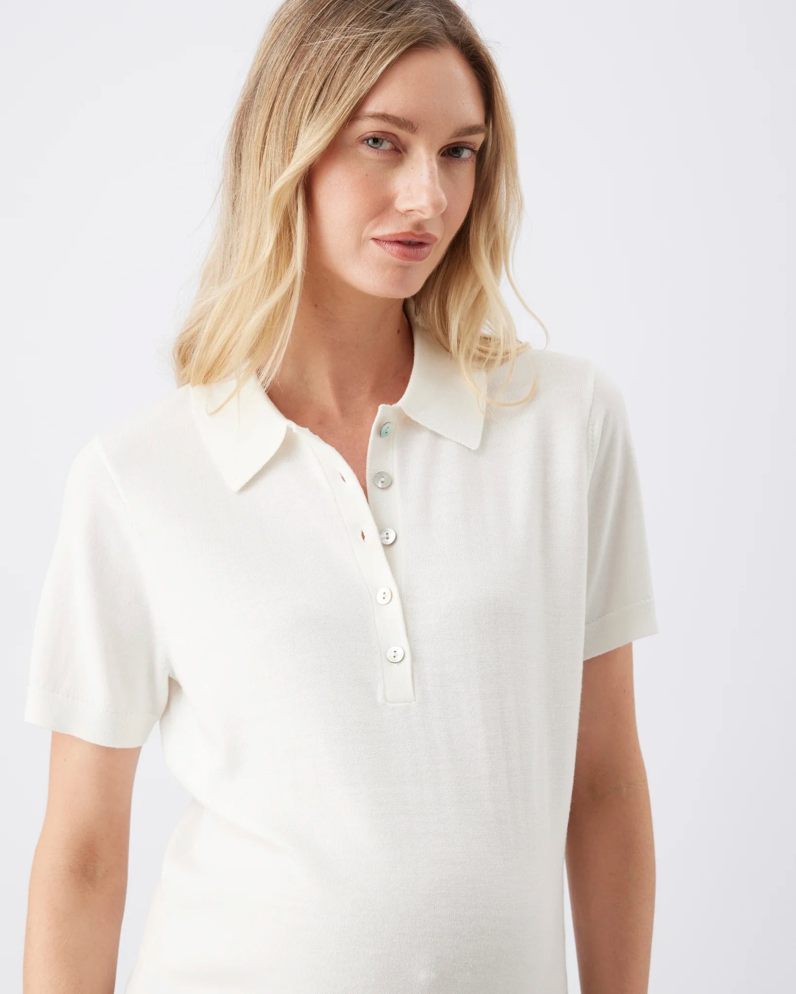 A woman wearing a short-sleeve polo shirt in off-white, photographed against a plain light gray studio background.