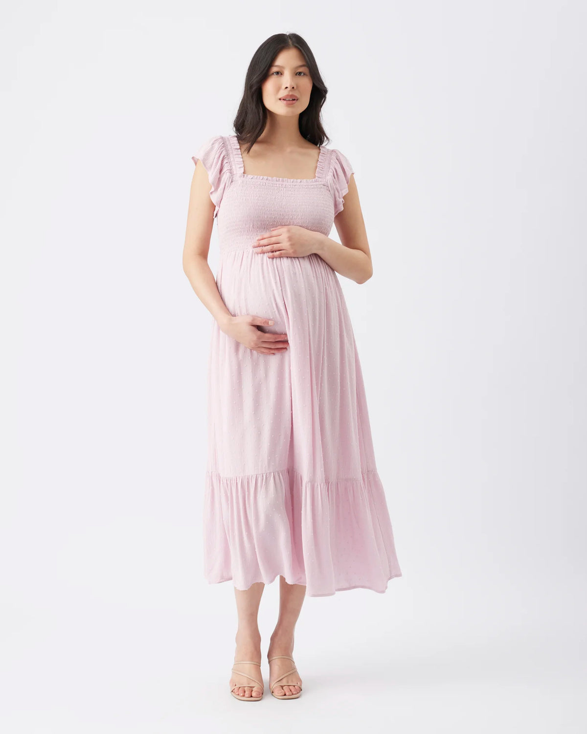 A pregnant woman modeling a light pink tiered maxi maternity dress with ruffled cap sleeves and a square neckline, standing against a plain white studio background.