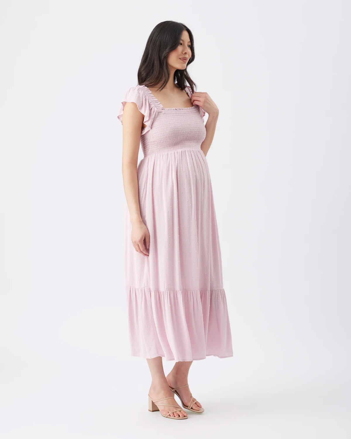 A woman modeling a light pink midi dress with ruffled cap sleeves, a square neckline, and a tiered skirt, photographed against a plain white studio background.