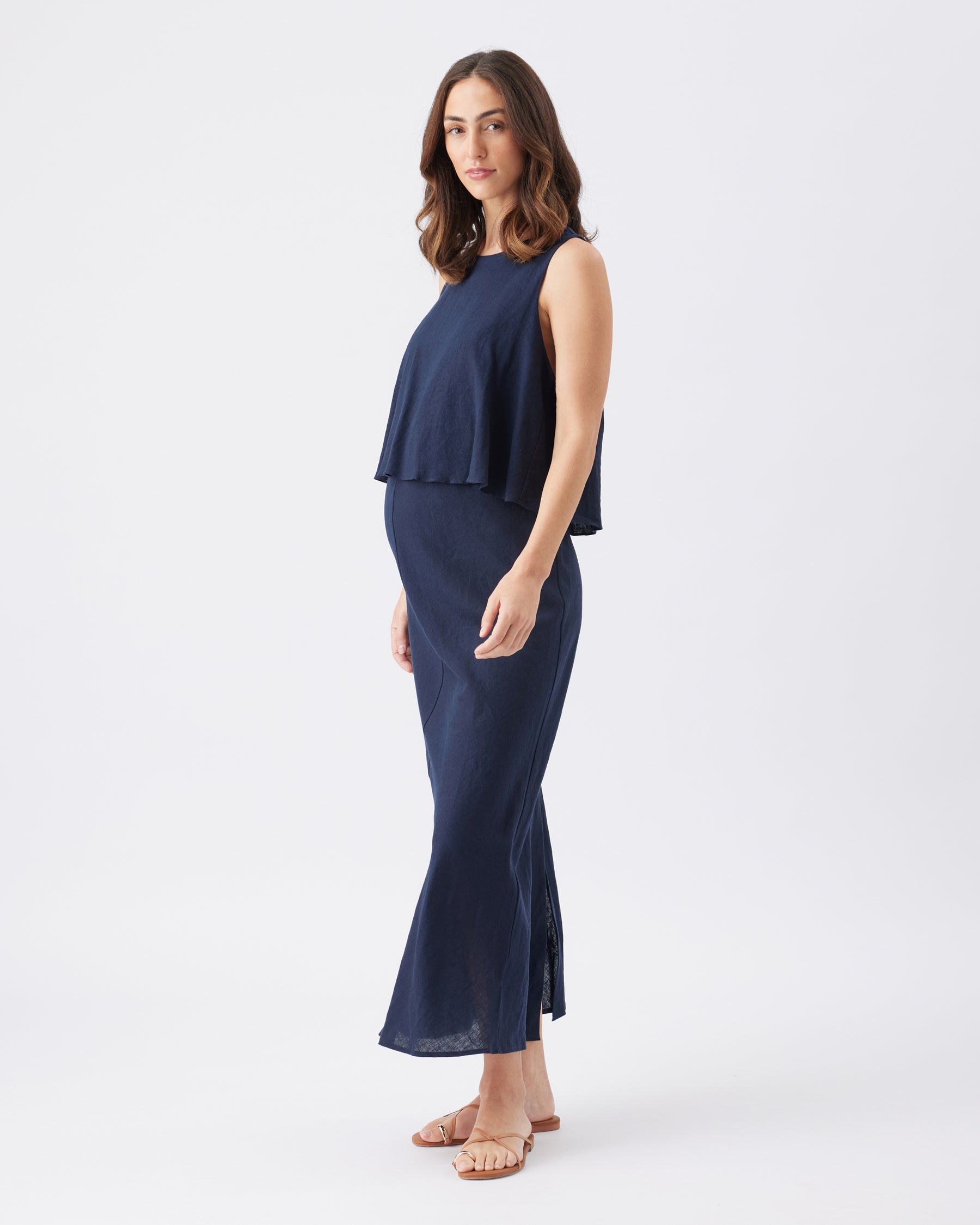 Side view of a pregnant woman wearing a navy blue sleeveless maxi dress on a white background