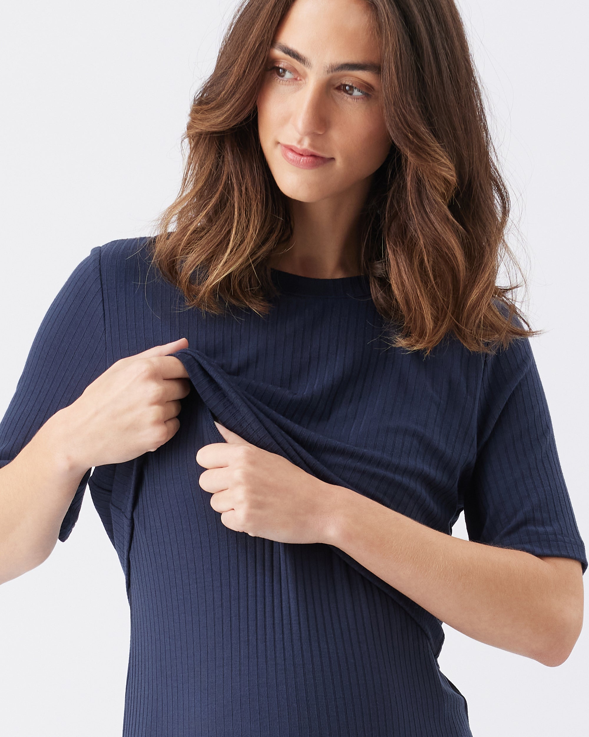 Woman wearing a navy blue ribbed dress and showing the nursing access against a white background