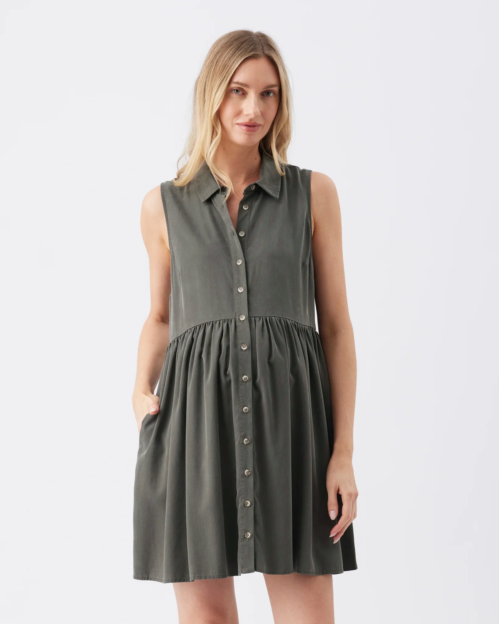 A woman modeling a sleeveless, dark gray button-down dress with a gathered waist and side pockets, set against a plain light gray background.