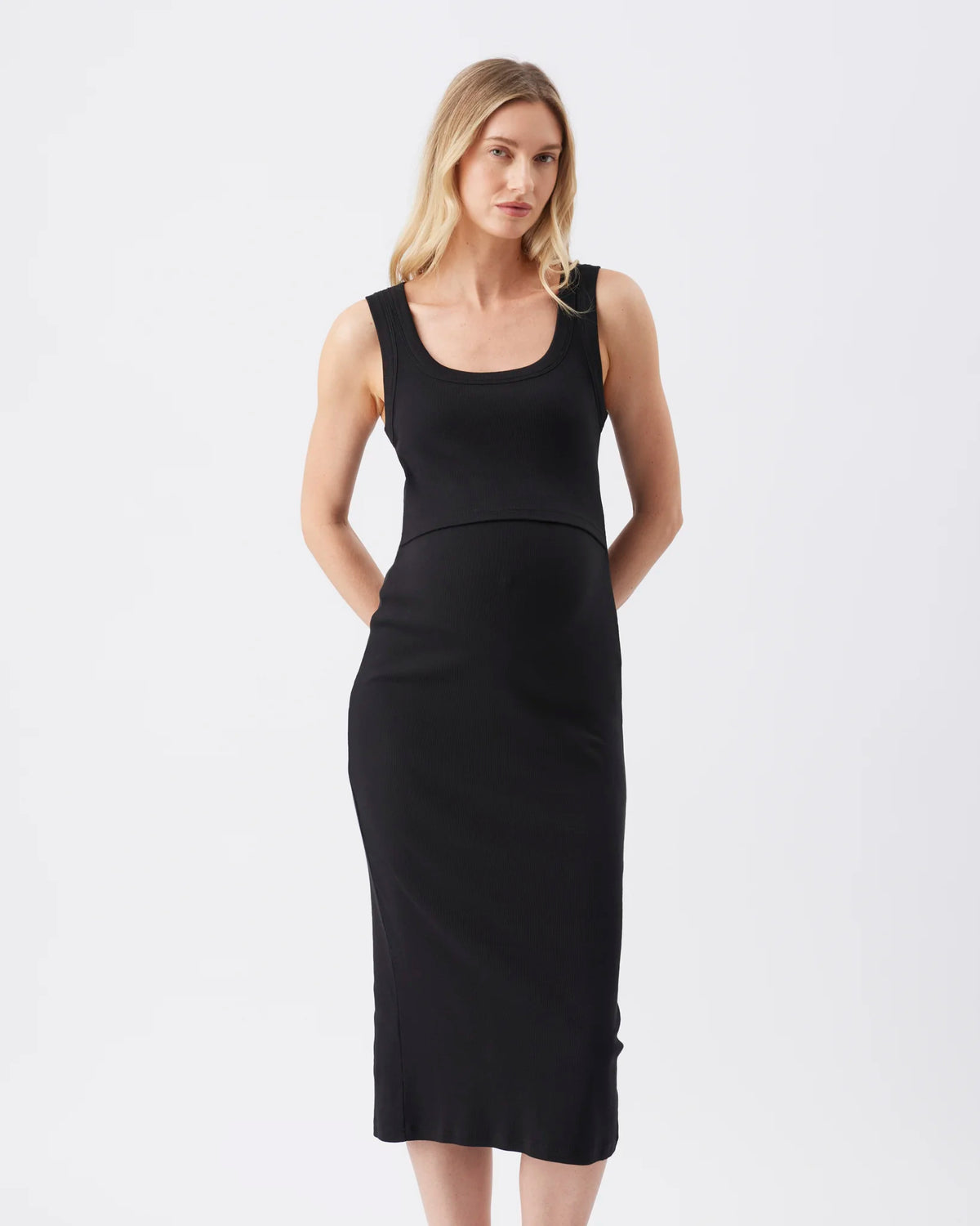 A woman modeling a sleeveless black midi dress with a scoop neckline and a fitted silhouette, photographed against a plain light gray studio background.