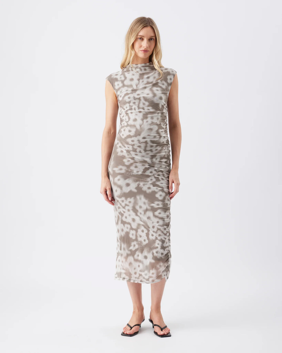 A woman modeling a sleeveless, high-neck midi dress with a beige and white abstract animal-print pattern, standing against a plain white studio background.