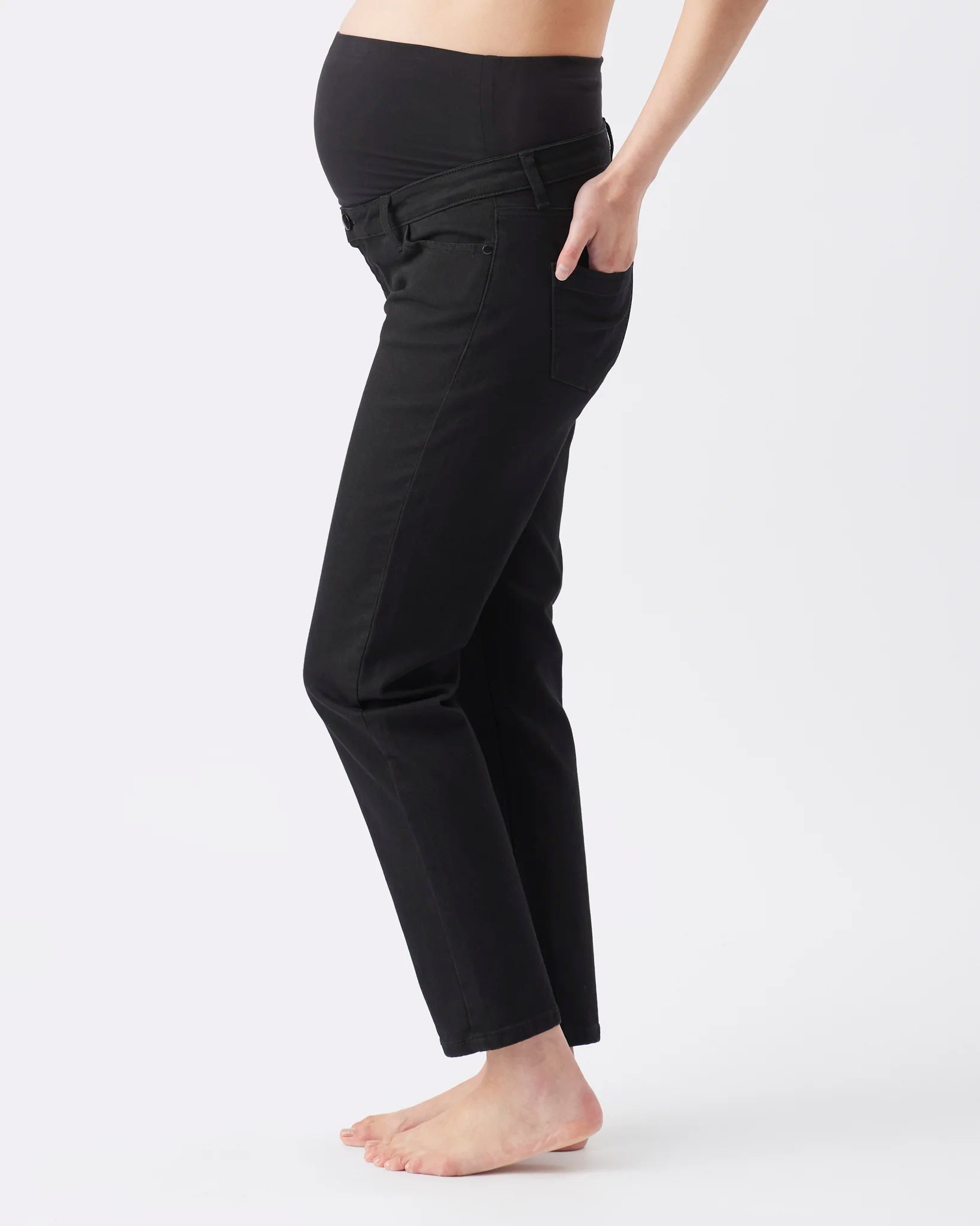 Black maternity pants shown on a model from the side, featuring a high elastic waistband and side pockets, against a plain white studio background.