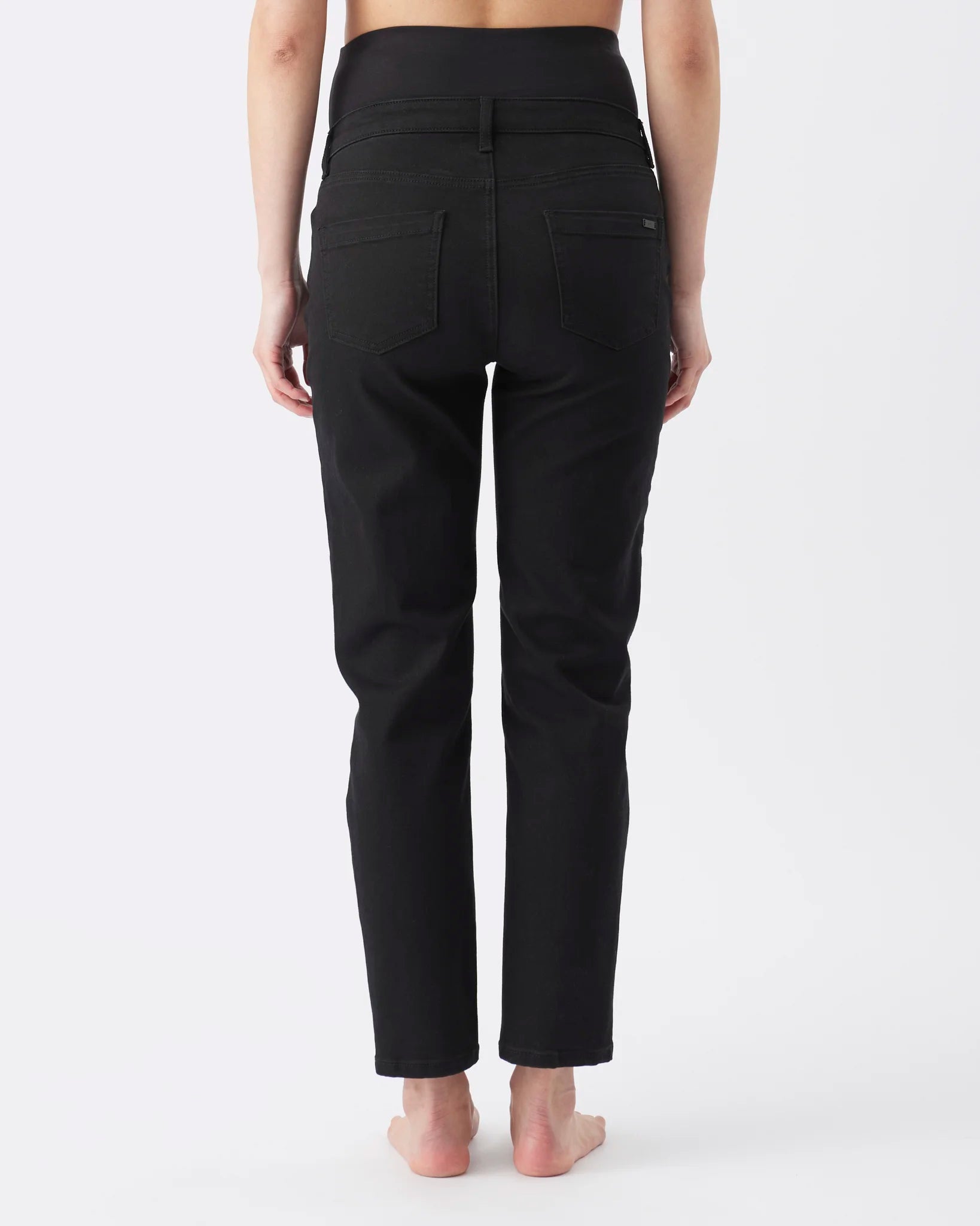 Rear view of a person wearing black high-waisted ankle-length pants against a plain light gray studio background.