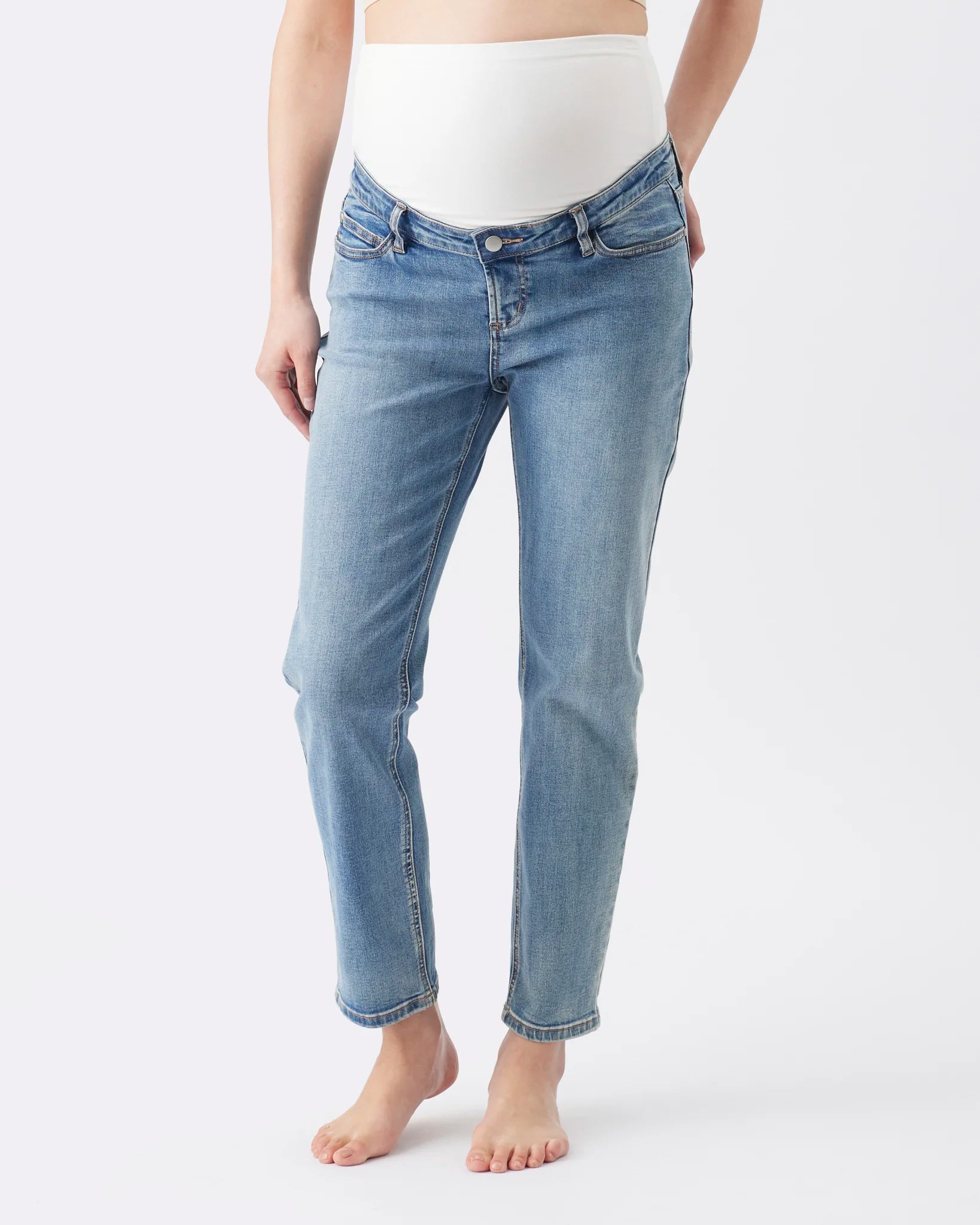 A model wearing light blue maternity jeans with a white maternity belly band, shown from the waist down on a plain white studio background.