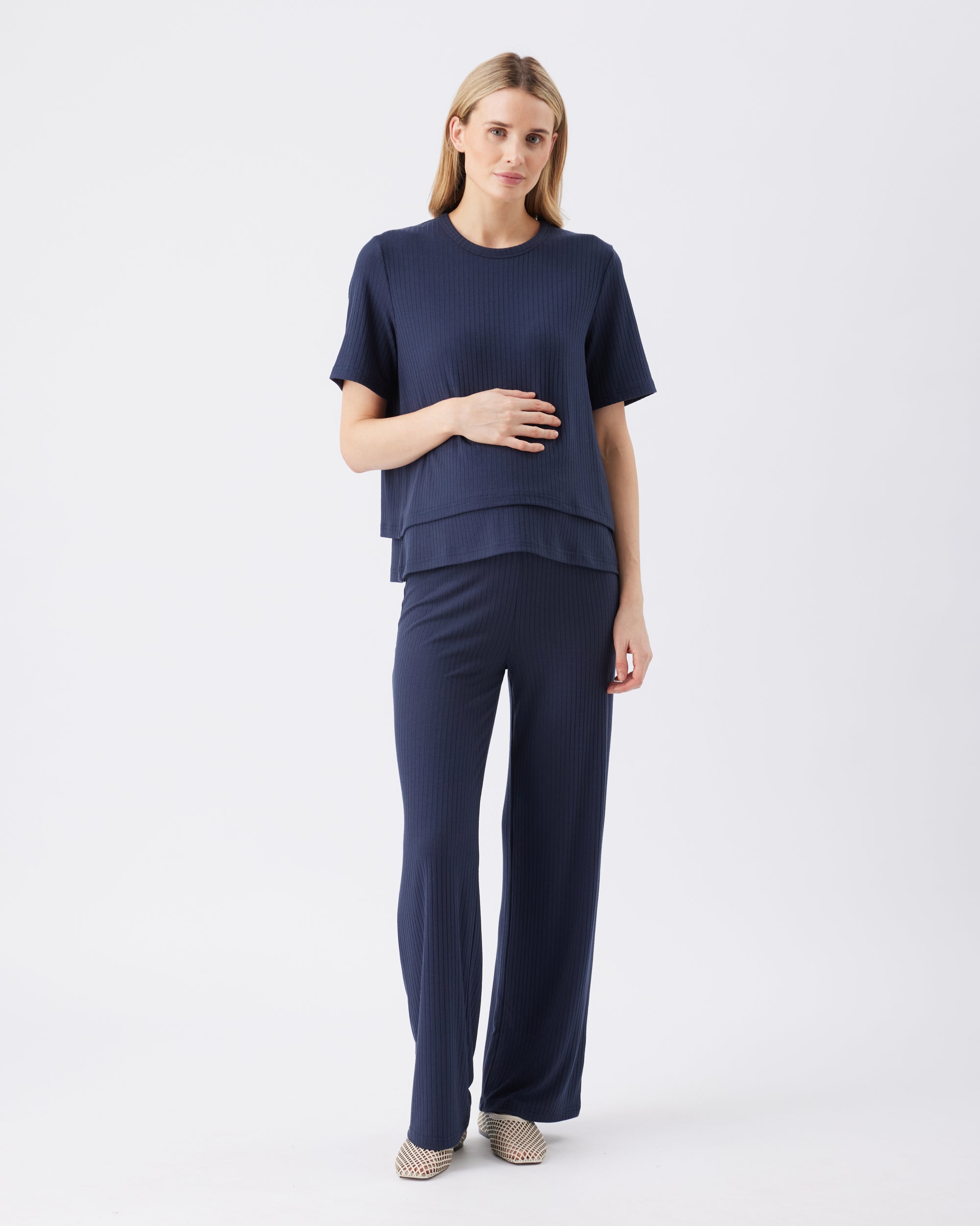 Full length shot of a woman wearing a navy outfit with a top and pants on a white background