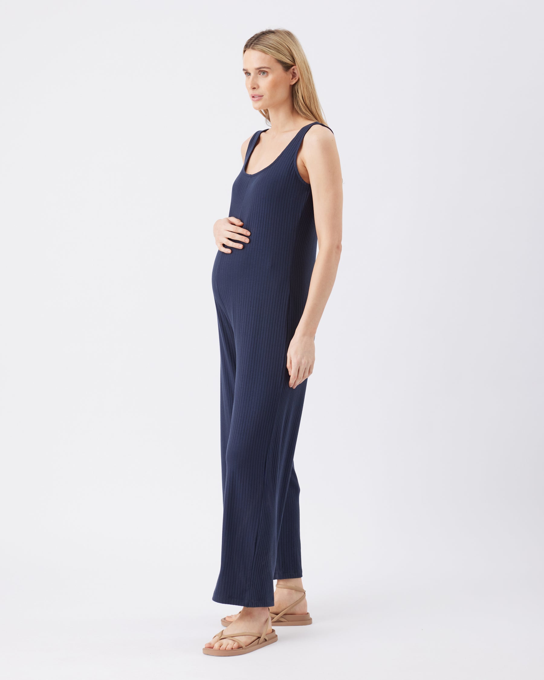 Side view of a pregnant woman wearing a navy blue sleeveless jumpsuit on a white background