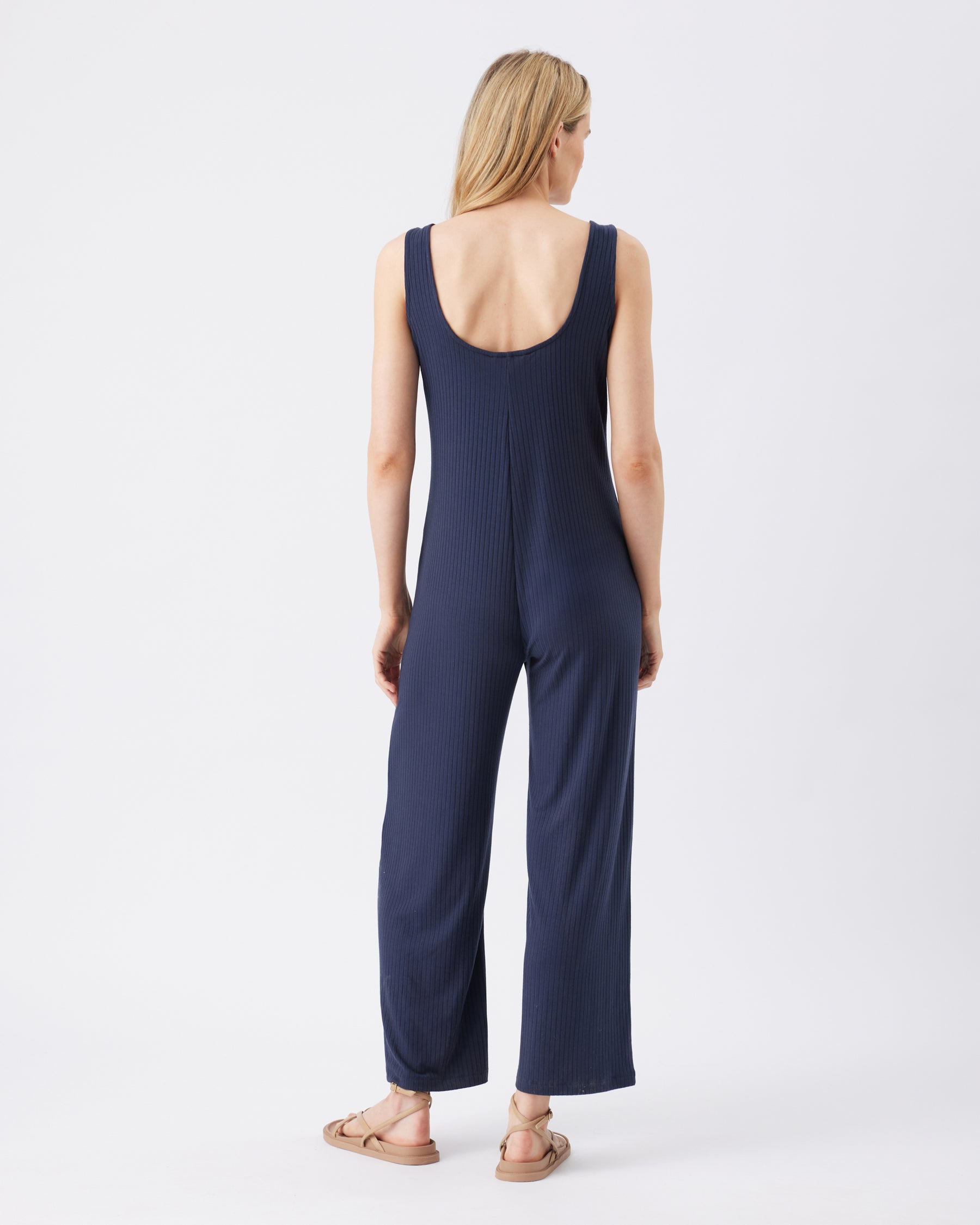 Back view of a woman wearing a navy blue jumpsuit on a white background