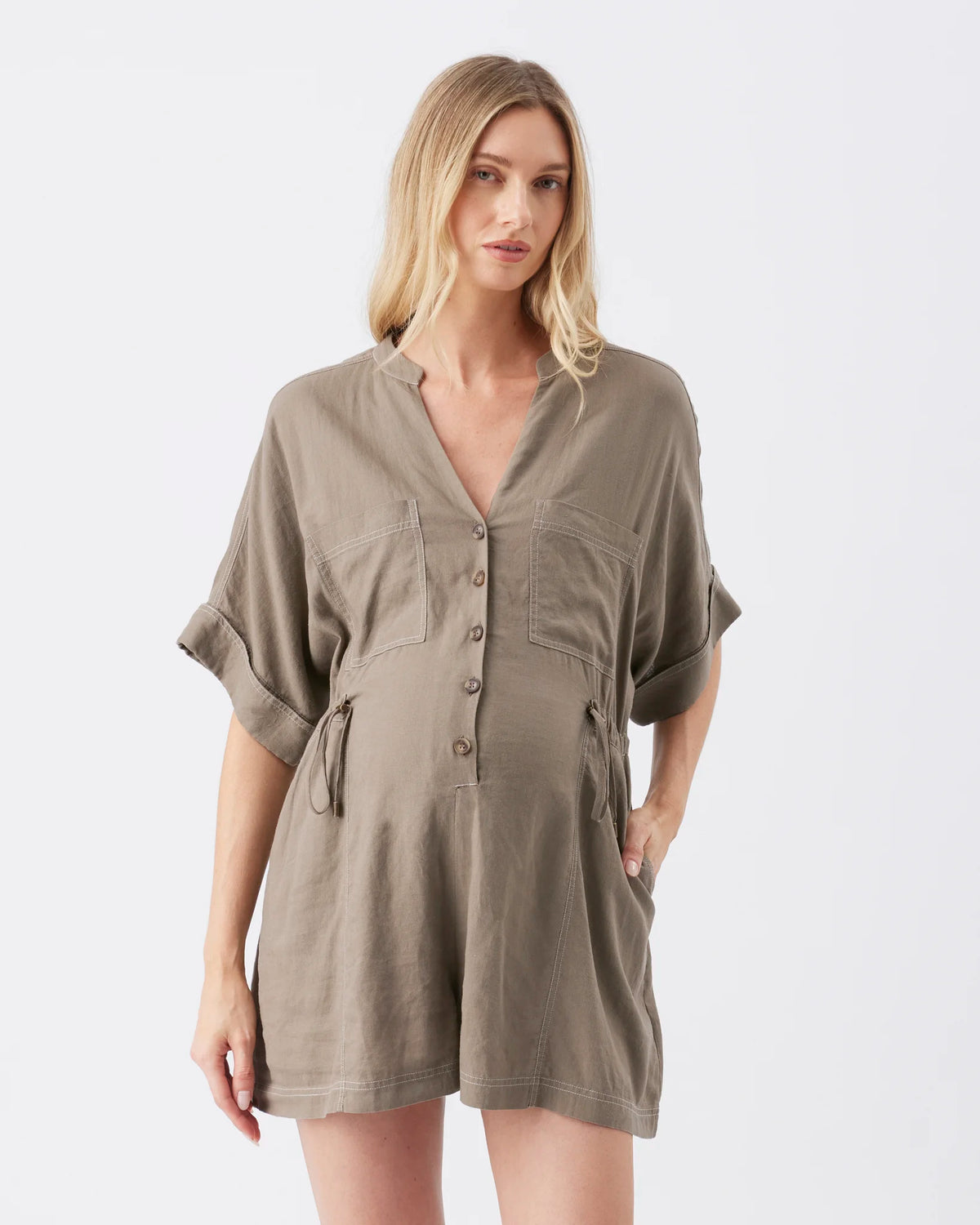 A woman modeling a short-sleeve, button-front romper in a muted taupe-brown color against a plain light gray studio background.