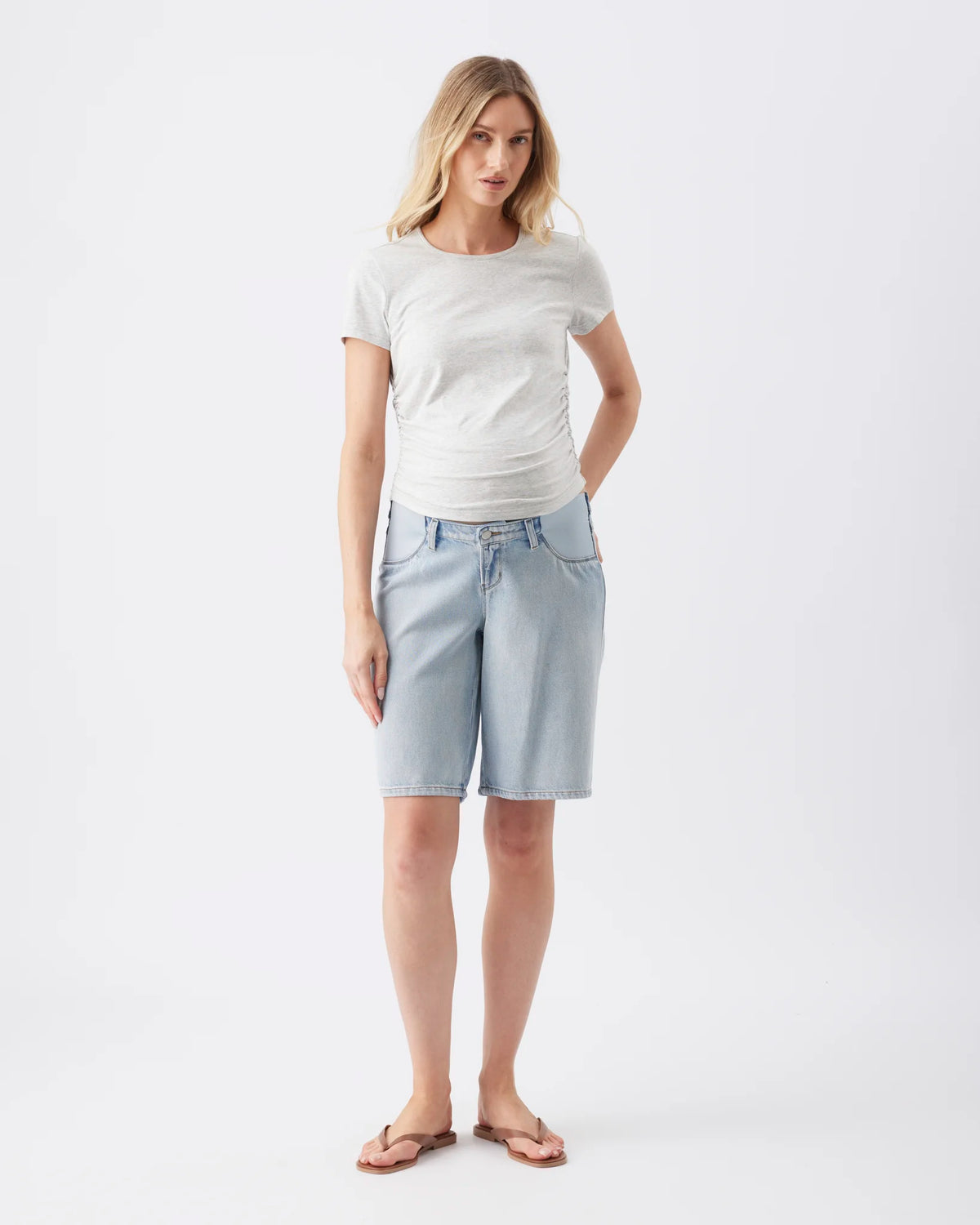 A woman modeling a light gray short-sleeve t-shirt and light blue denim shorts against a plain white studio background.