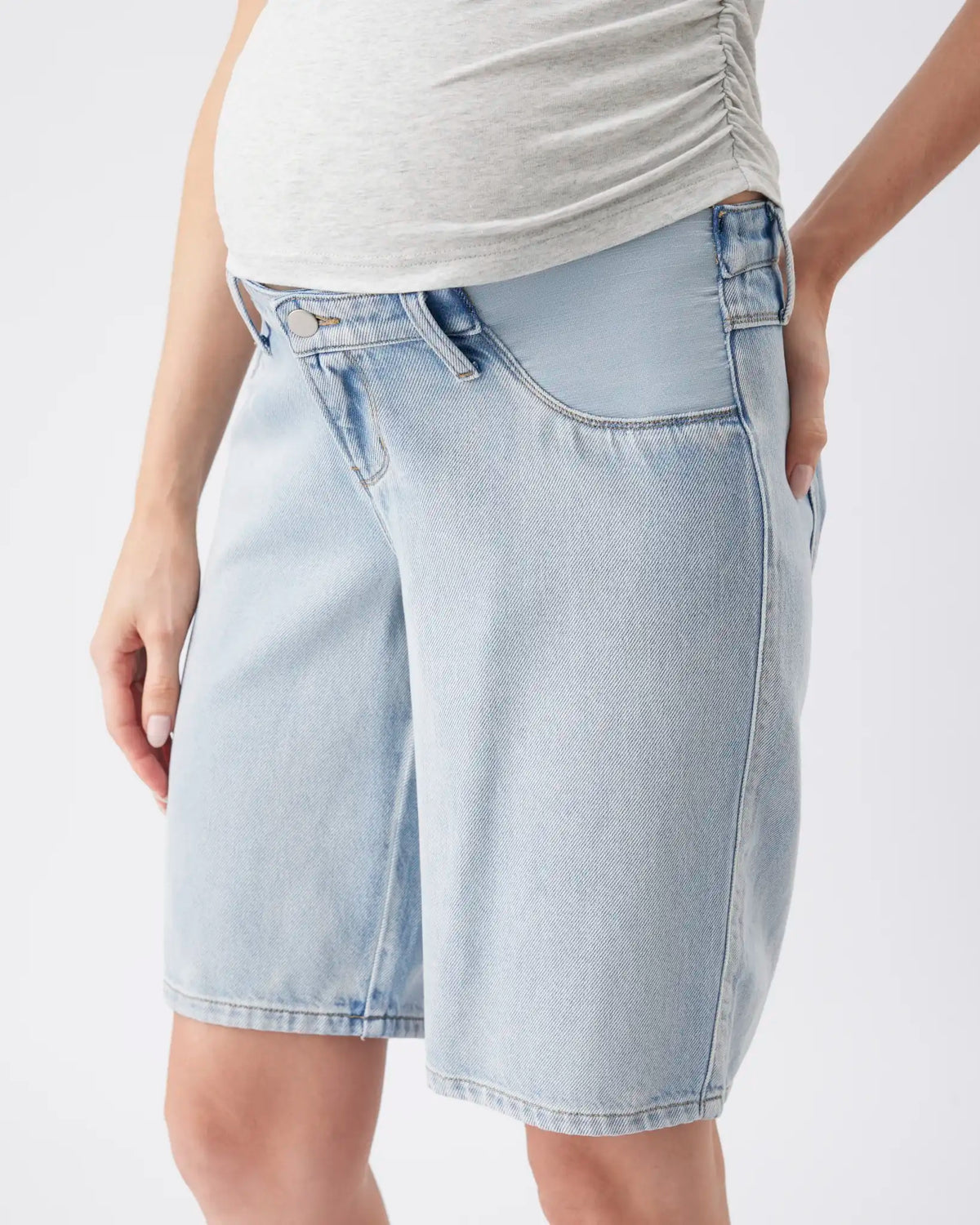 A close-up of a model wearing light-wash blue denim shorts with a gathered waistband, paired with a light gray ruched top, against a plain white background.
