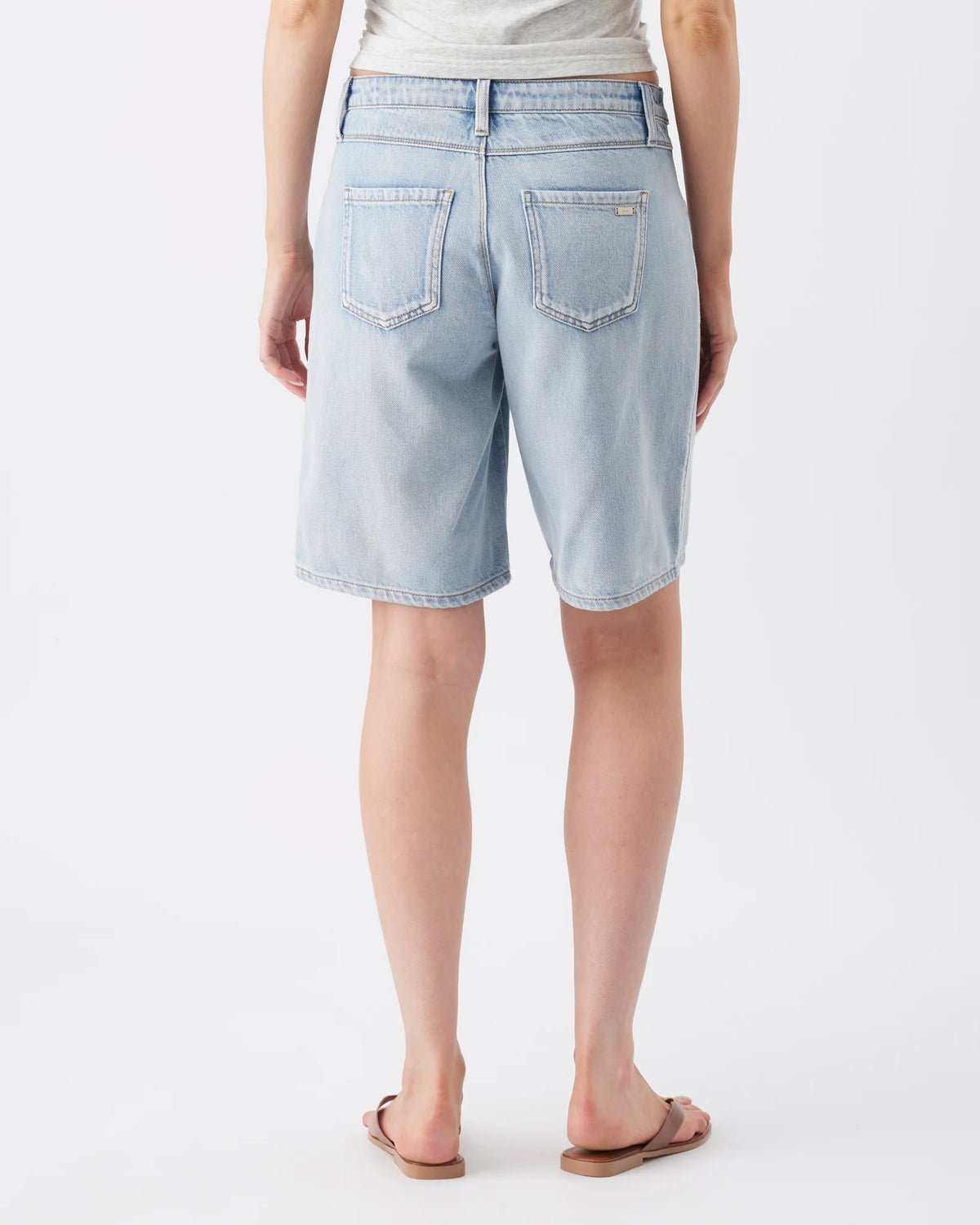 A person shown from the back wearing light-wash denim shorts, a light heather gray top, and brown flip-flop sandals against a plain white studio background.
