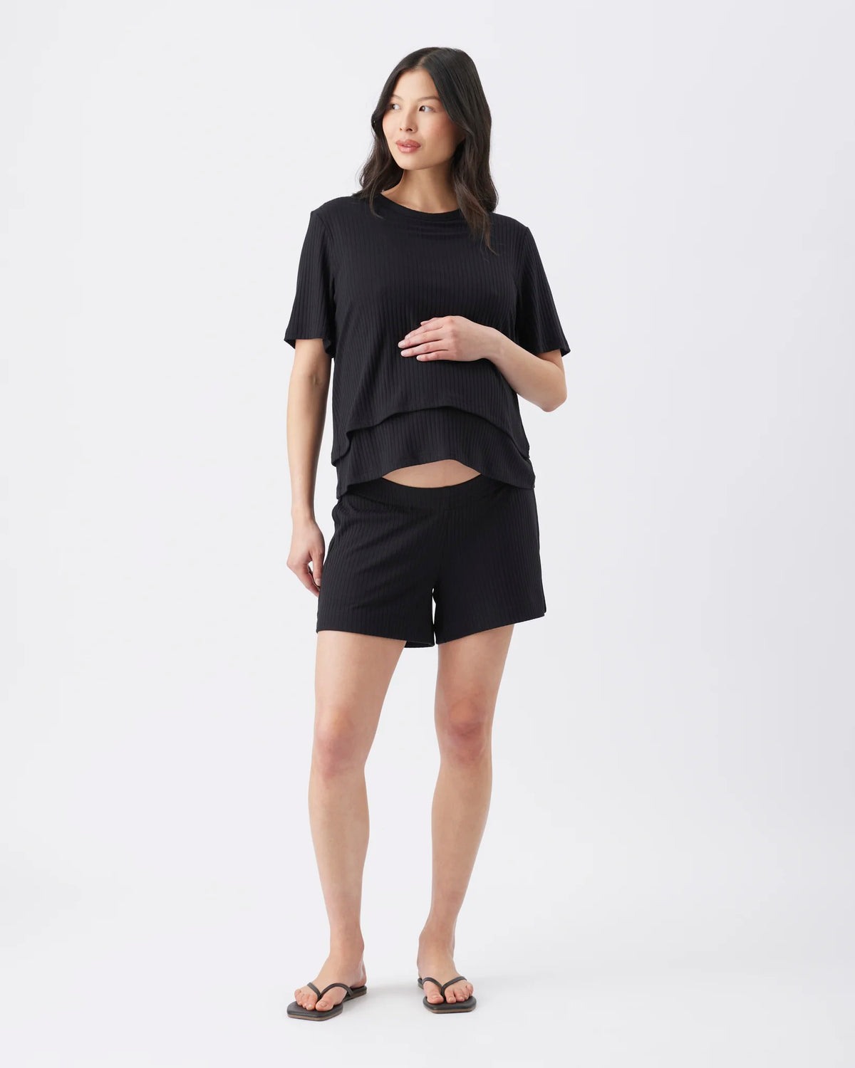 A woman modeling a black short-sleeve layered t-shirt and matching black shorts against a plain white studio background.