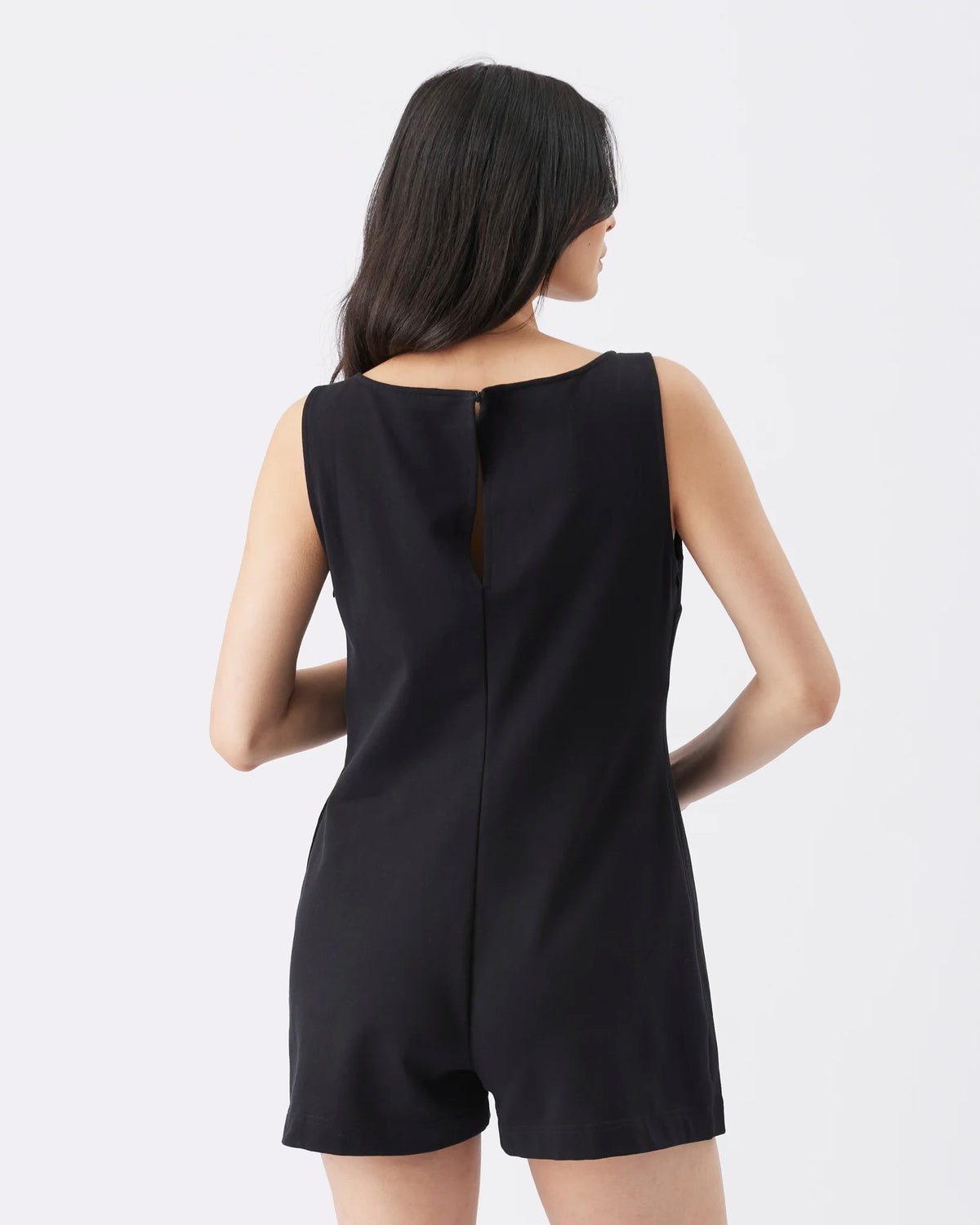 A woman shown from the back wearing a black sleeveless romper against a plain light gray studio background.