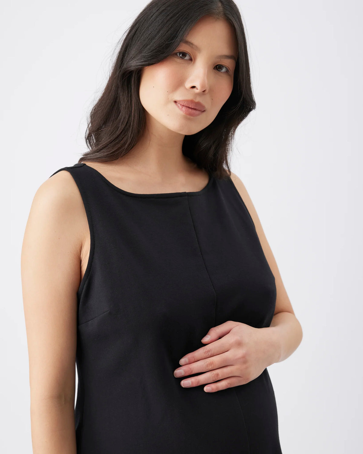 A woman wearing a sleeveless black top with a scoop neckline, photographed against a plain light gray studio background.