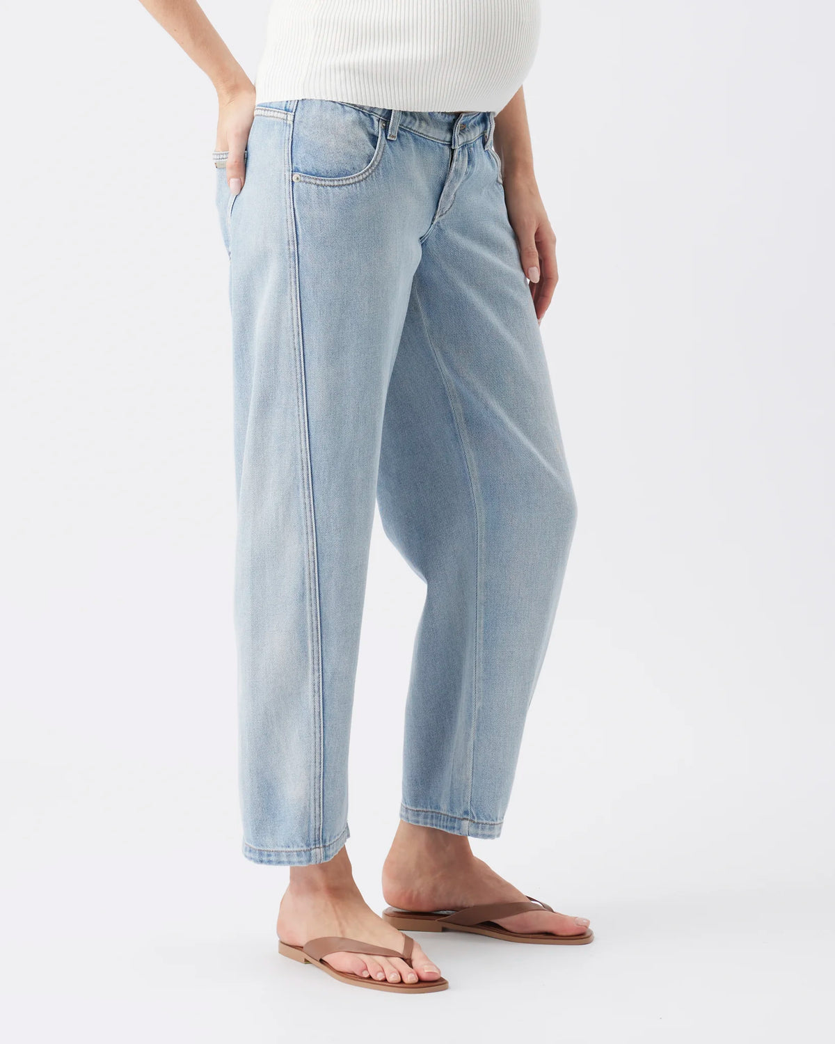 A person wearing light-wash blue cropped jeans with a relaxed straight-leg fit, paired with a white ribbed top and brown flip-flop sandals, photographed against a clean white studio background.