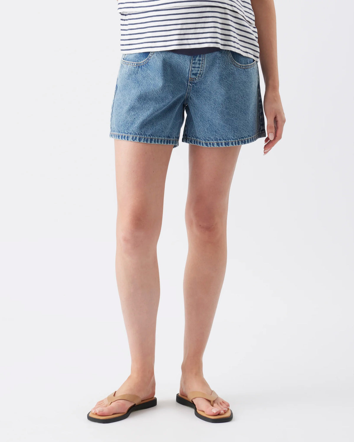 A model from the waist down wearing light-wash blue denim shorts, a navy and white striped top, and brown sandals, photographed against a clean white studio background.