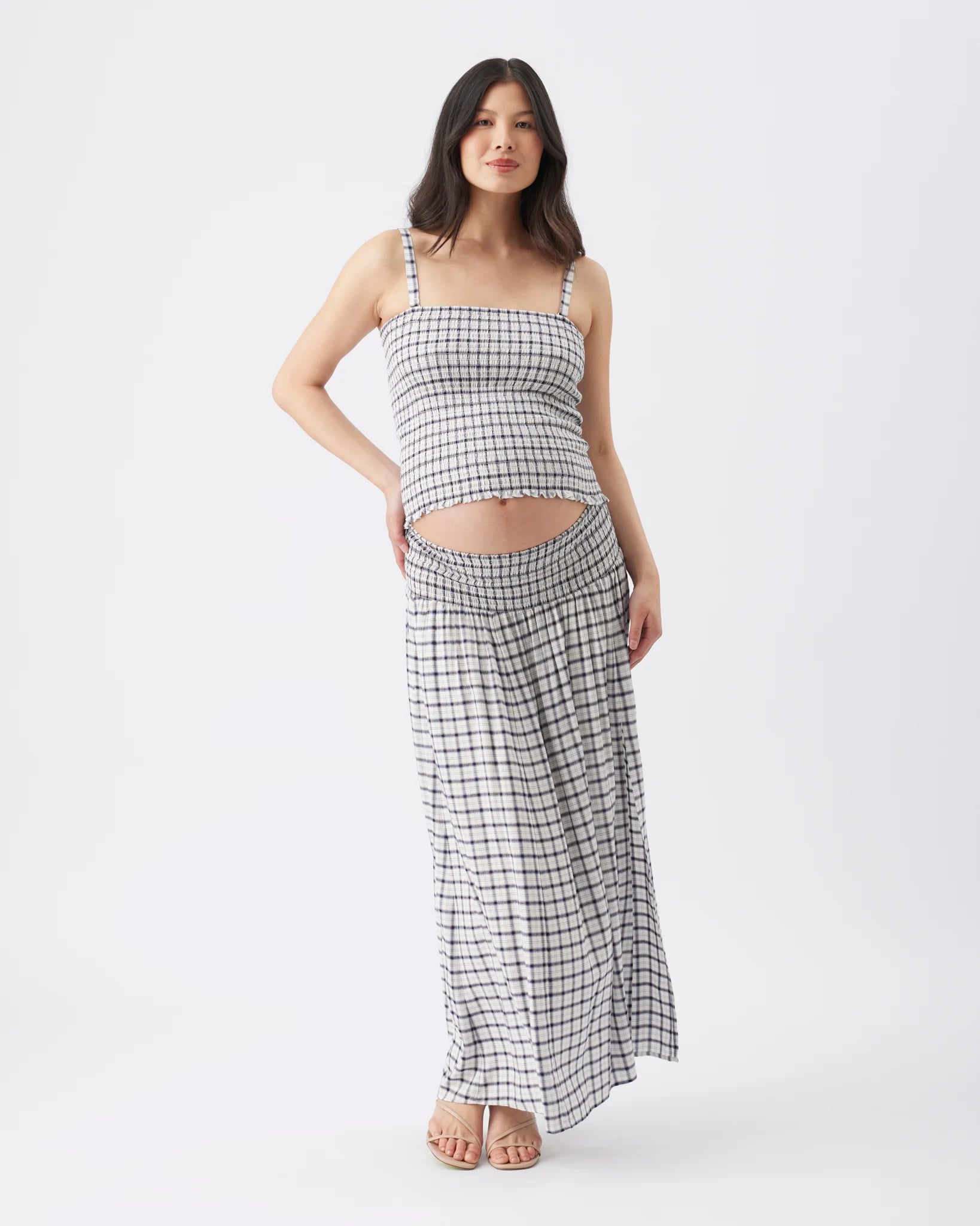 A woman modeling a matching two-piece set consisting of a black and white checkered crop top and high-waisted maxi skirt, photographed against a seamless white studio background.