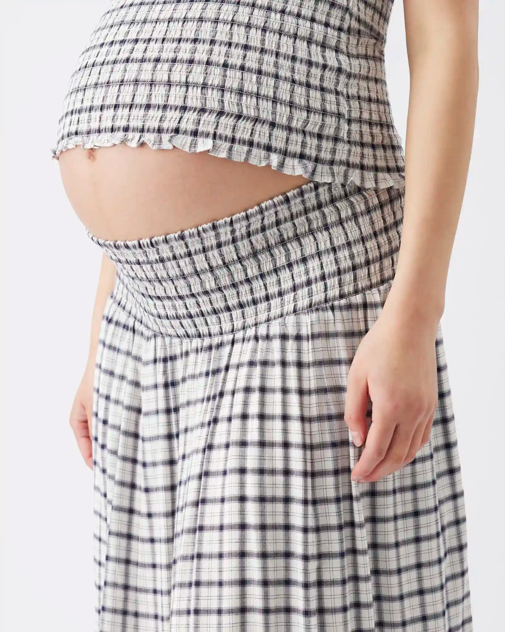 A close-up of a pregnant model wearing a matching smocked maternity top and skirt set in a black and white gingham pattern.
