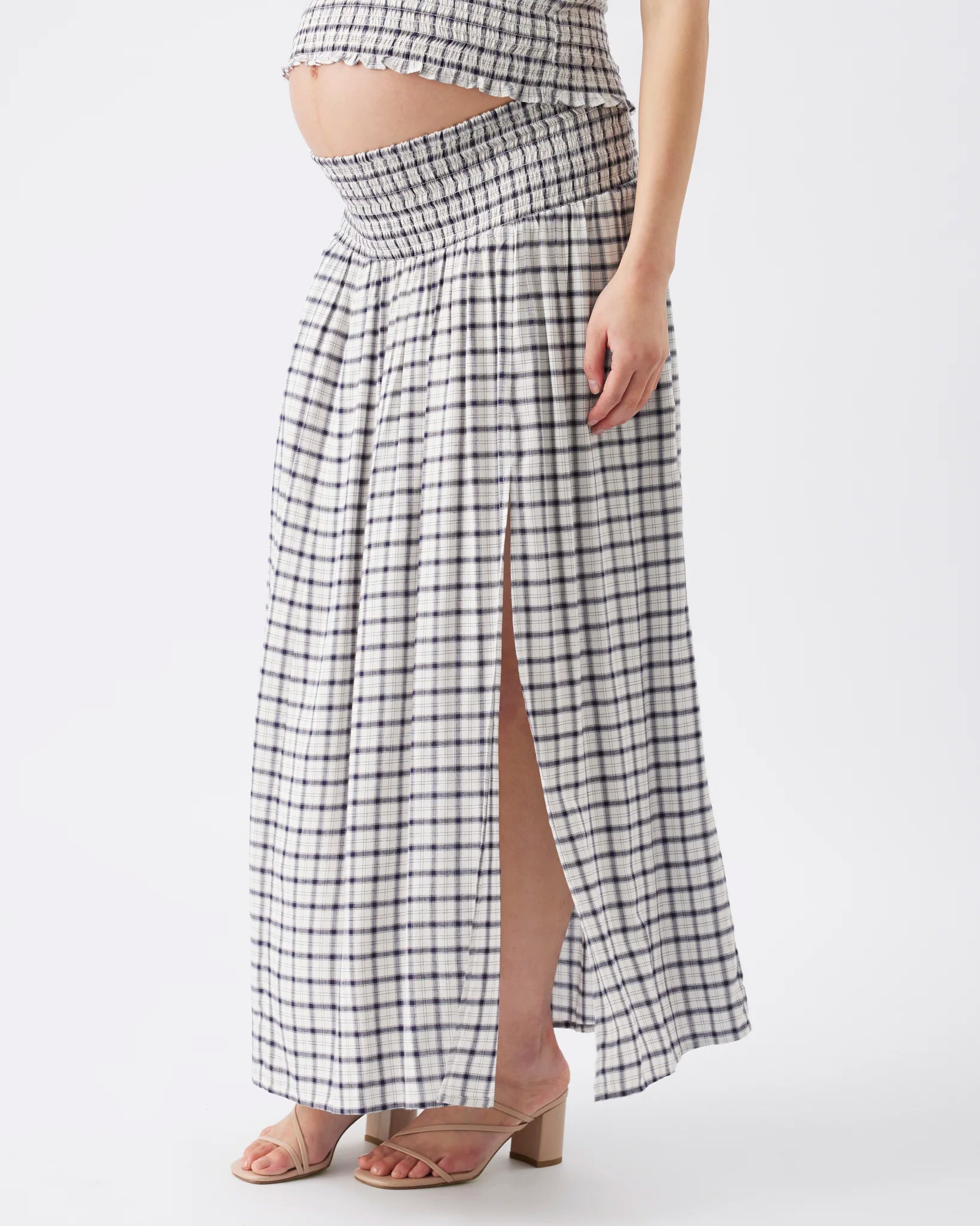 A model wearing a black and white checkered maxi skirt with a high side slit, paired with clear heeled sandals, shown against a plain white studio background.