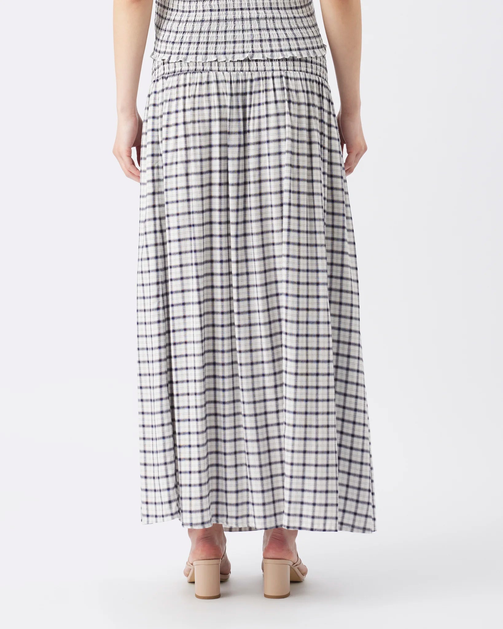 A woman wearing a long white maxi skirt with a black and gray gingham check pattern, shown from the back against a plain white studio background.